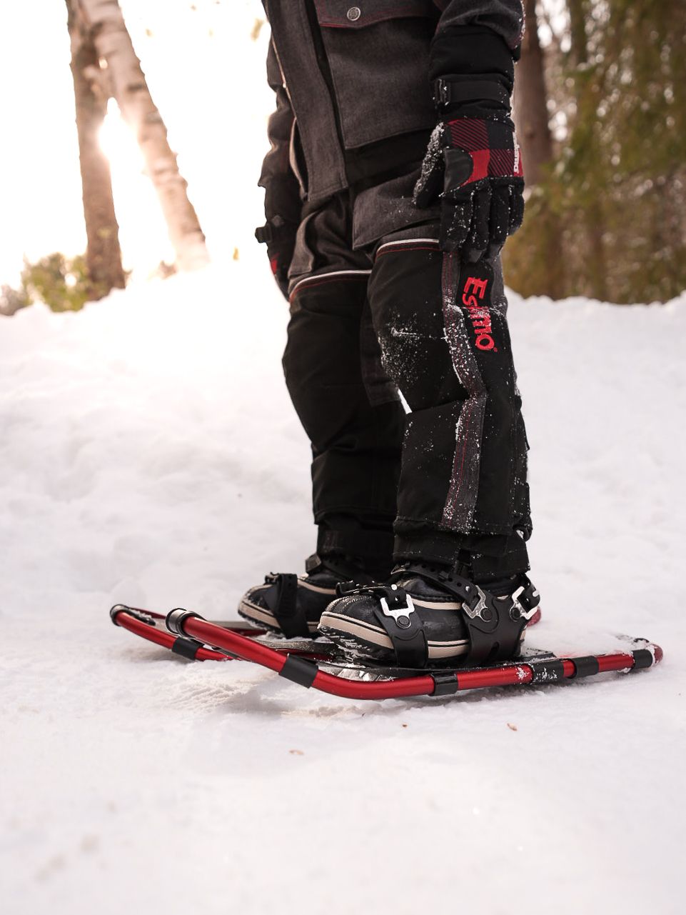 Close-up view of winter boots strapped into red snowshoes on fresh snow.