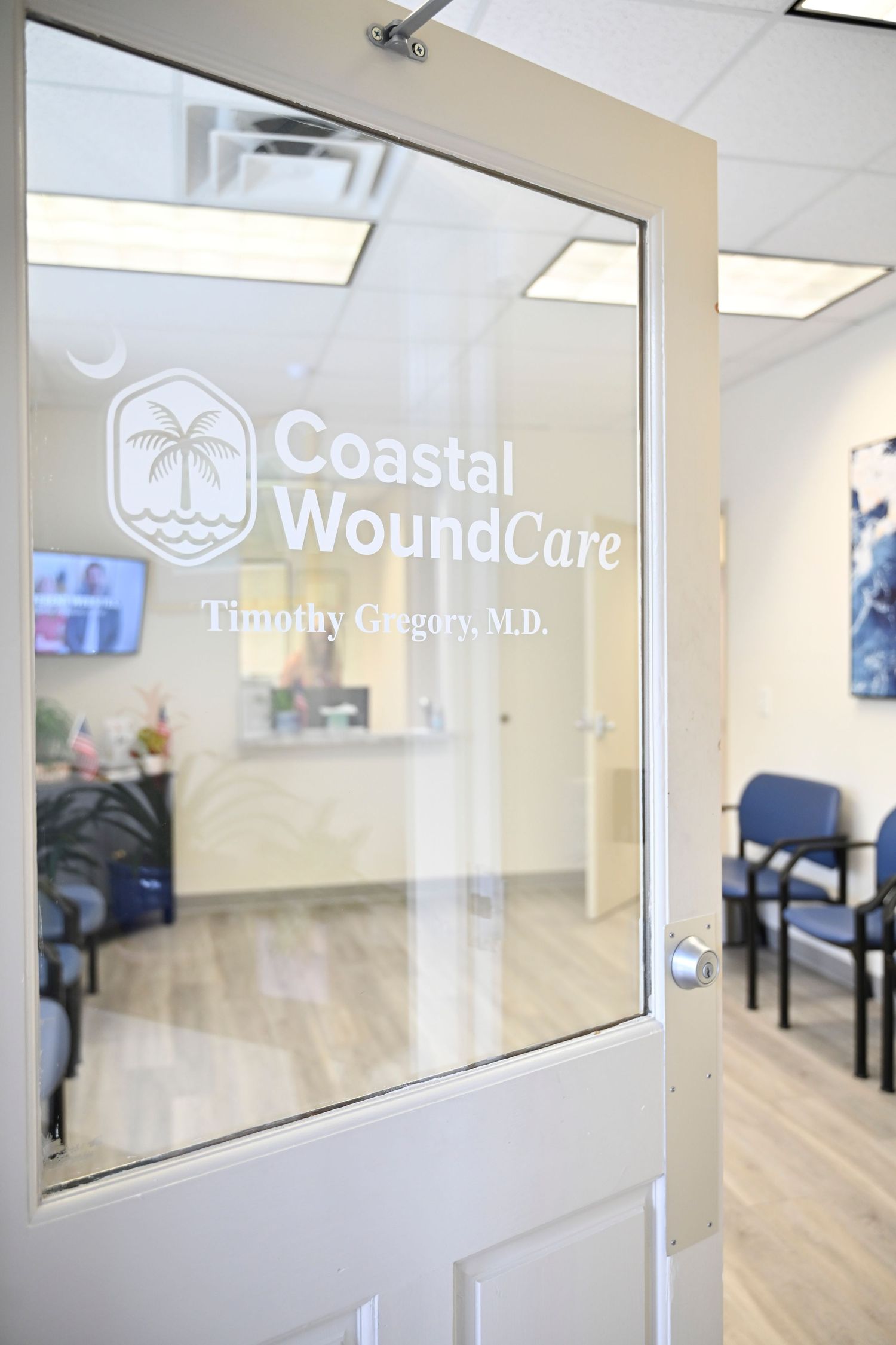 Glass door entrance to Coastal WoundCare medical office with palm tree logo and wood flooring visible inside.