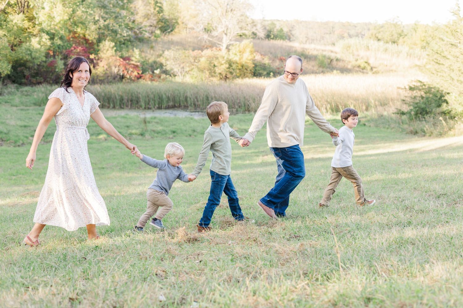 A family holds hands while walking together through a grassy field at sunset.