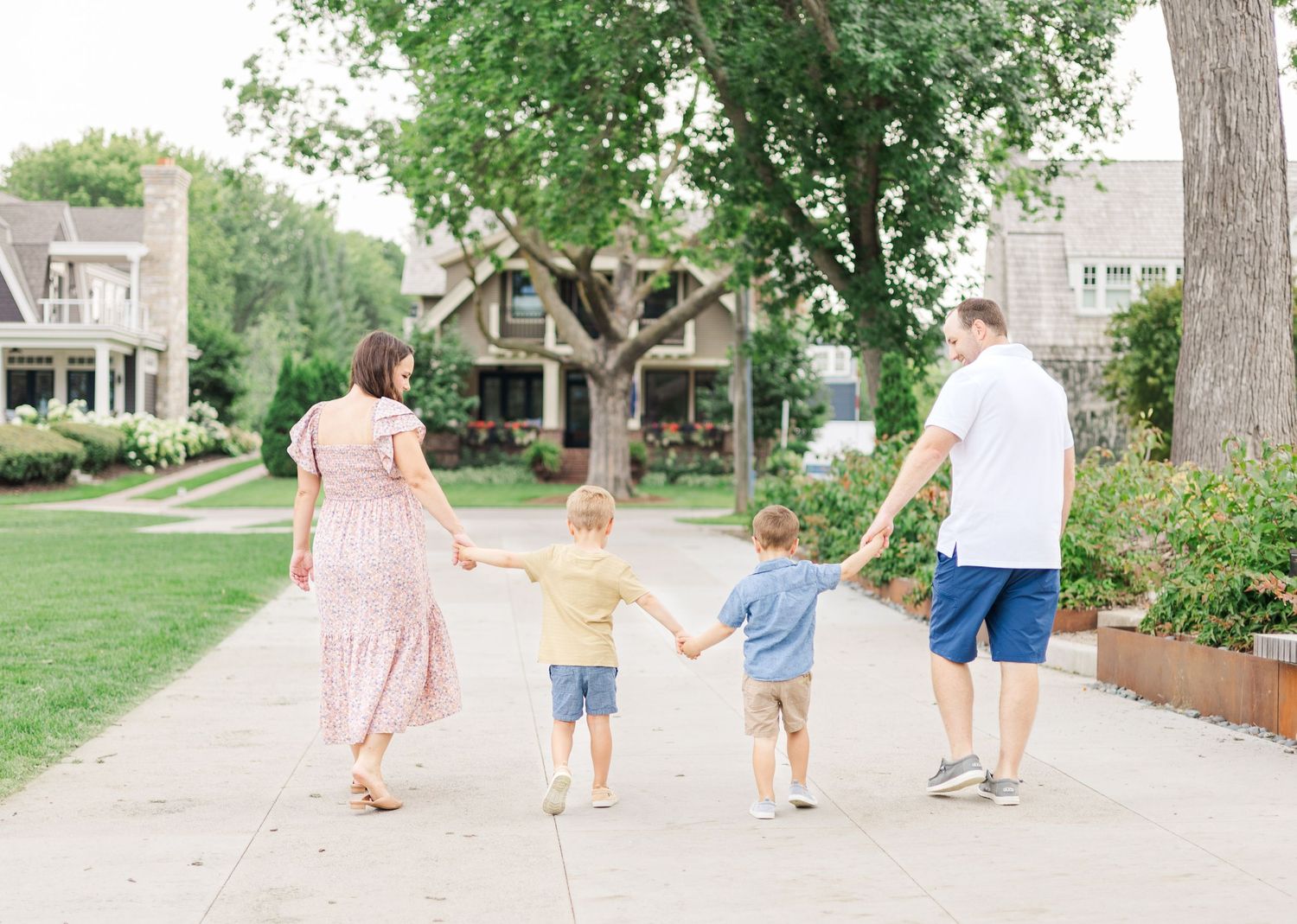 Family walking together on a tree-lined sidewalk holding hands on a sunny summer day.