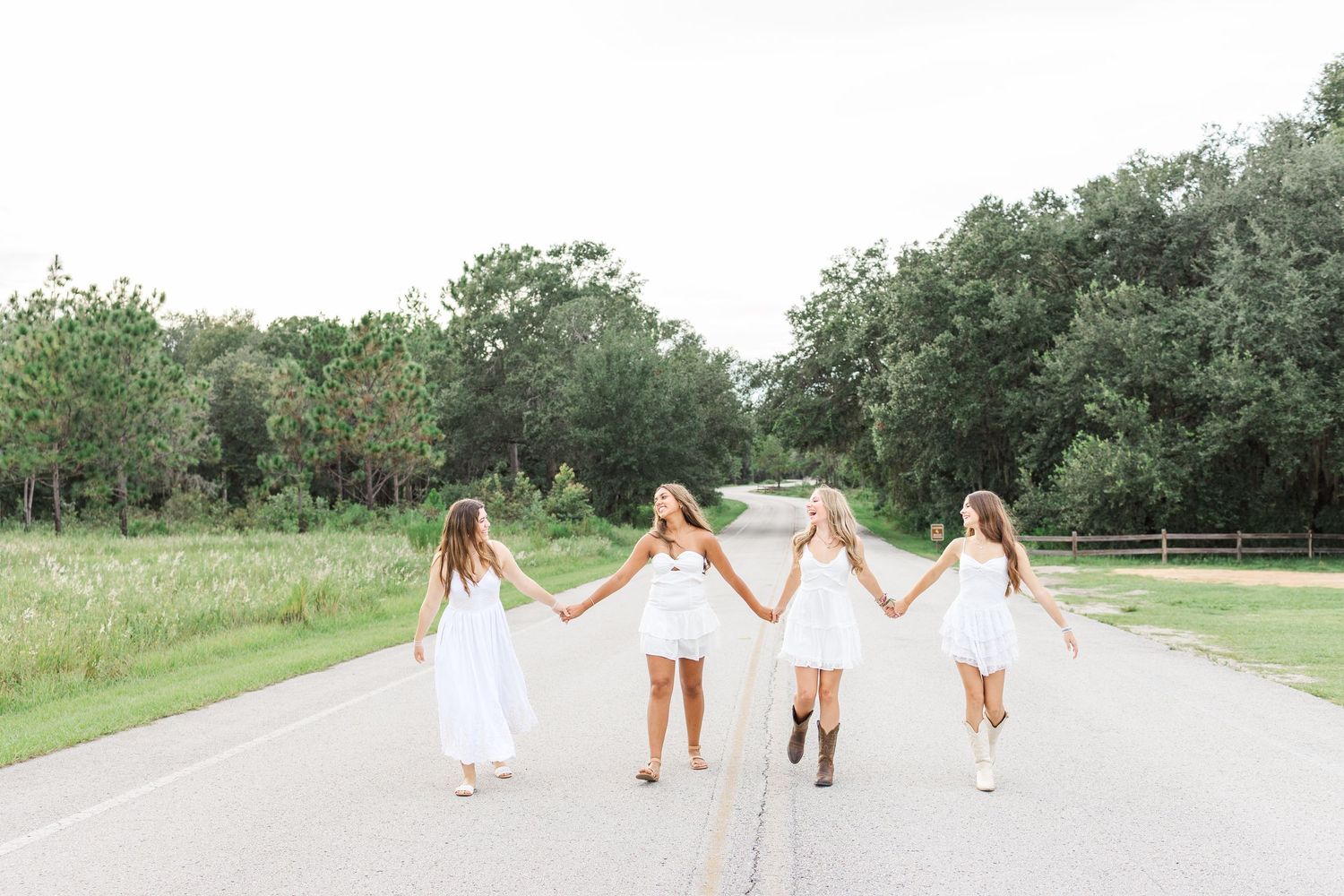 Group walking down rural path wearing white dresses creating dreamy summer scene.