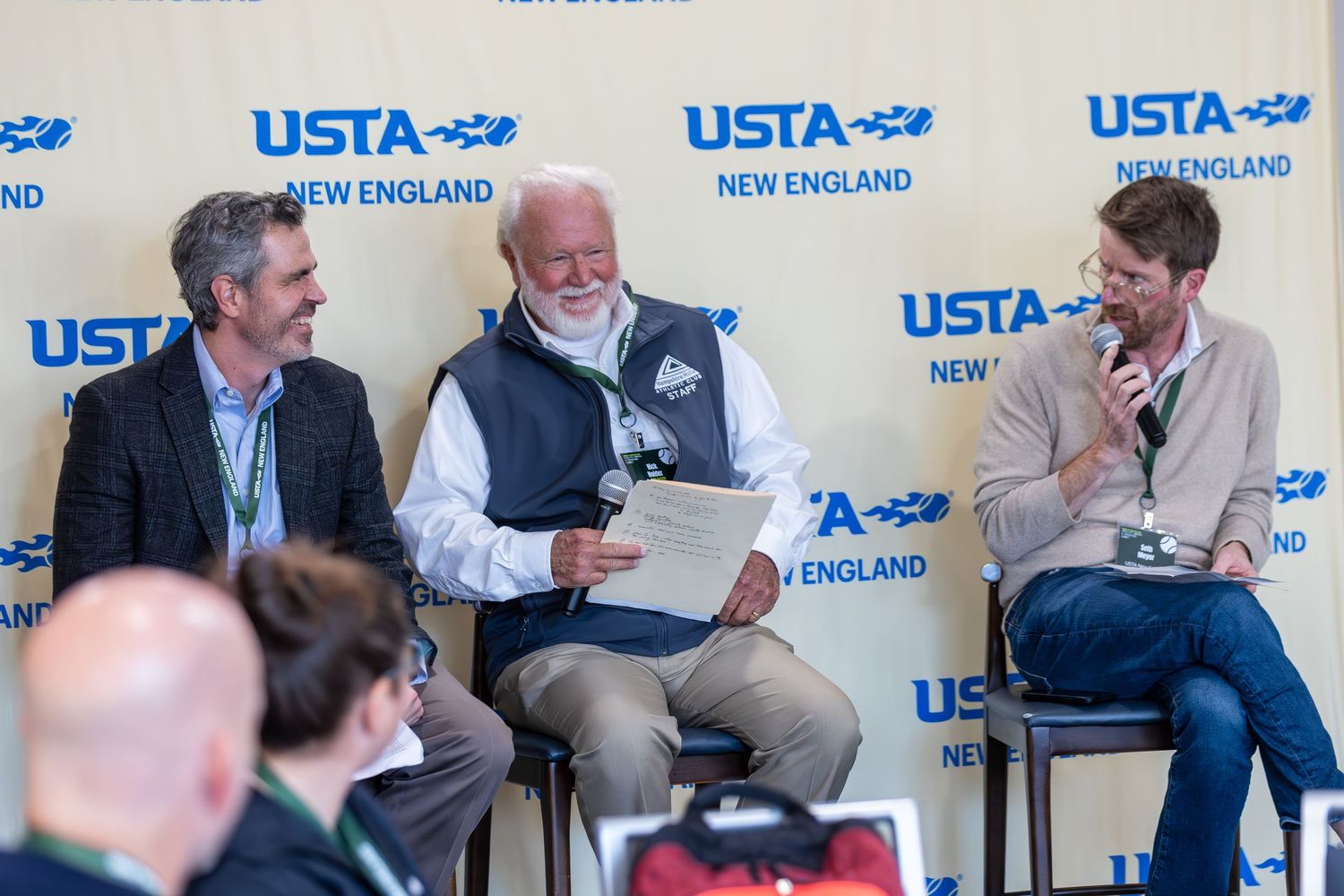 Panel discussion with speakers seated in chairs on stage at USTA New England event with branded backdrop.