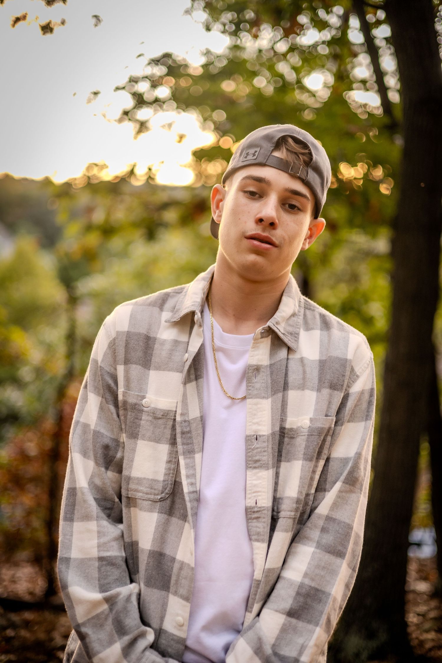 Young person in grey plaid flannel and baseball cap poses outdoors during golden hour sunset in autumn.