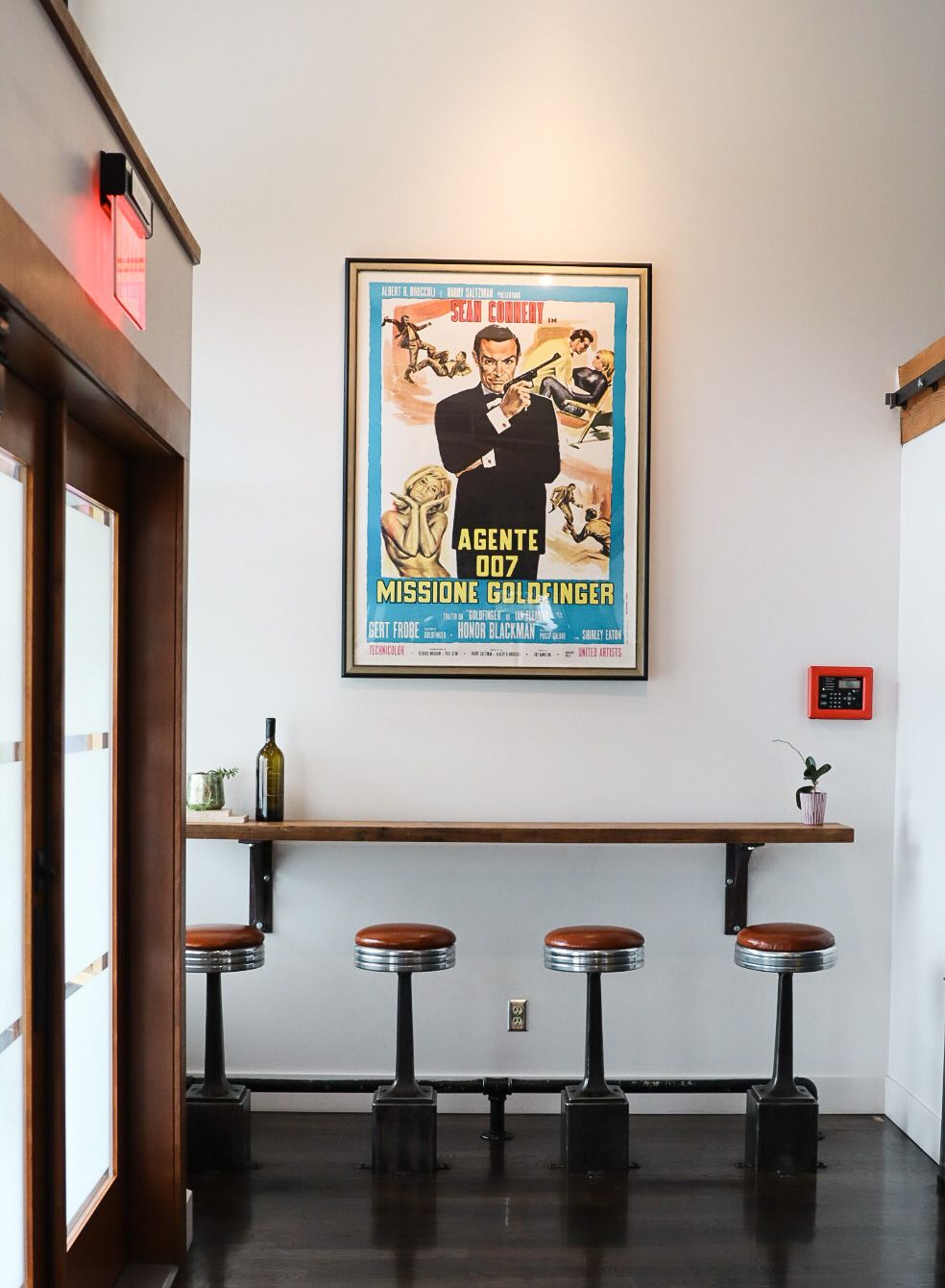 Minimalist bar area featuring retro movie poster and four industrial-style stools with leather seats.