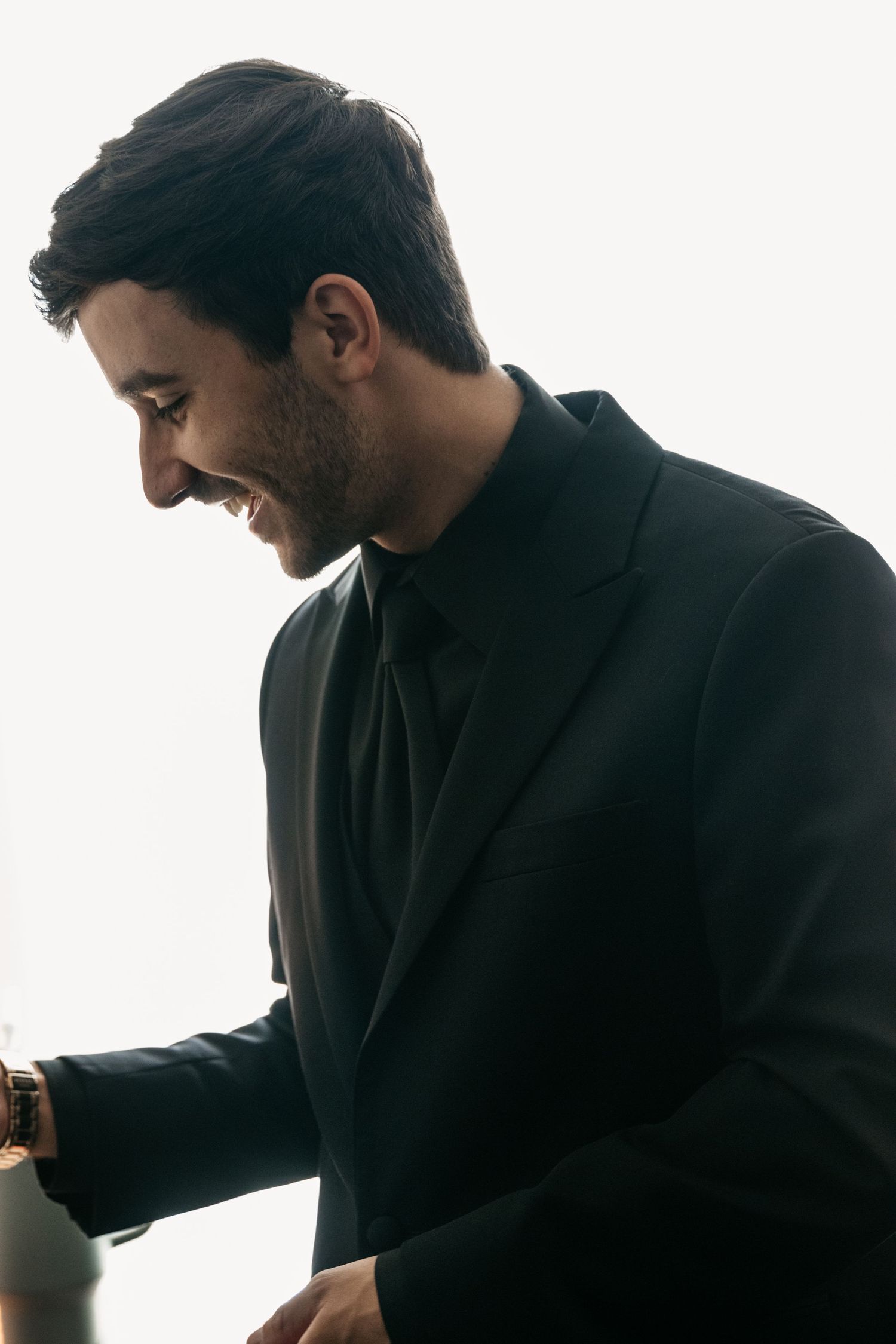 A person in a dark suit smiles while looking down in a shadowy profile portrait.
