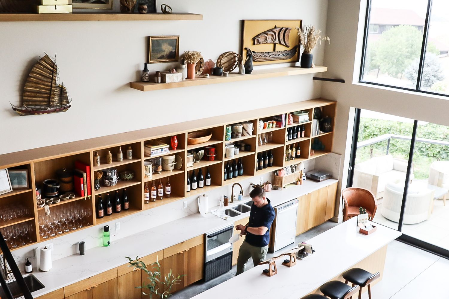 Modern bar interior with extensive wooden shelving displaying bottles and decor items near a window.