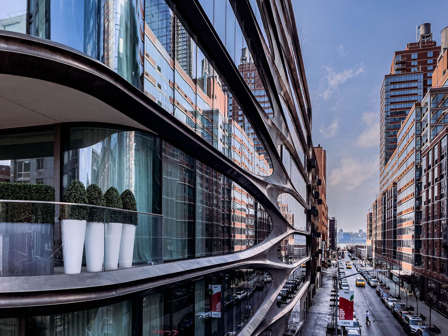 Modern glass office building facade with curved architecture and reflective windows along an urban street.
