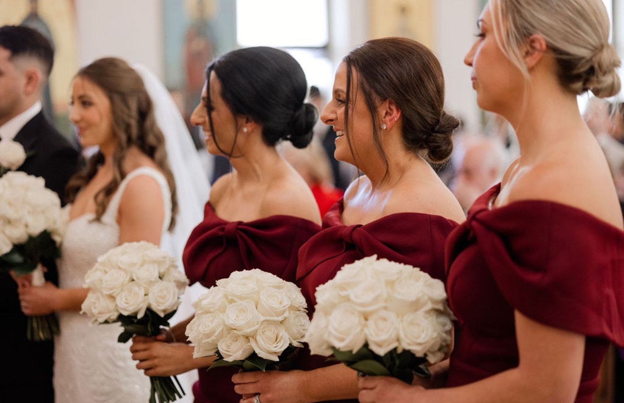 Bridesmaids bridal party in burgundy dresses all with soft curled low buns with curled face framing.
