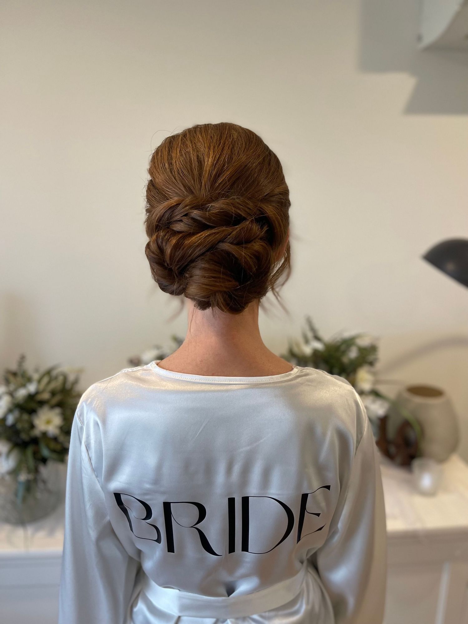 Red hair long and thick twisted into an elegant low bridal bun with a neat texture and soft face framing
