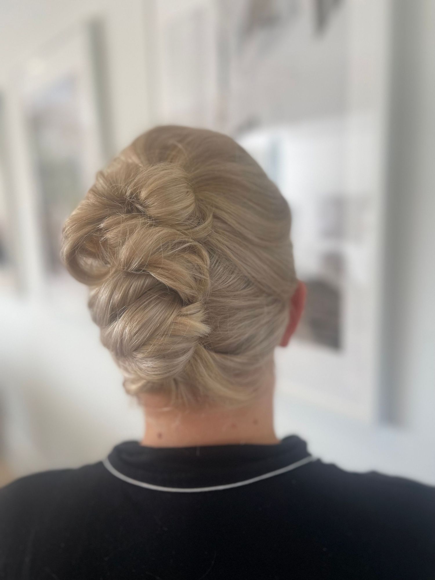 Short blonde hair curls and pinned into a high bun to give volume.