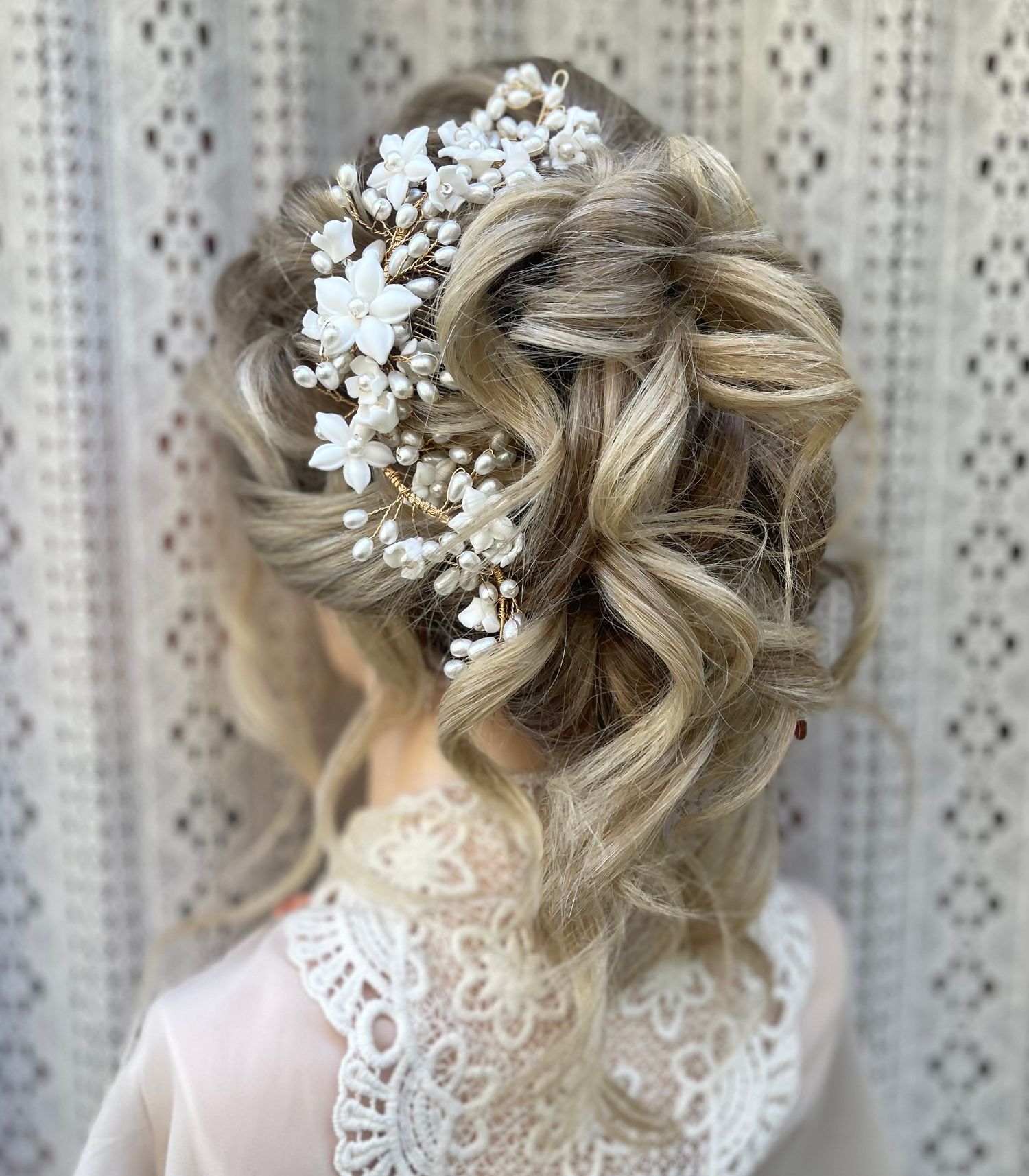 Very textured curly updo with loose curls hanging out detailed with a large floral and pearl hair accessory