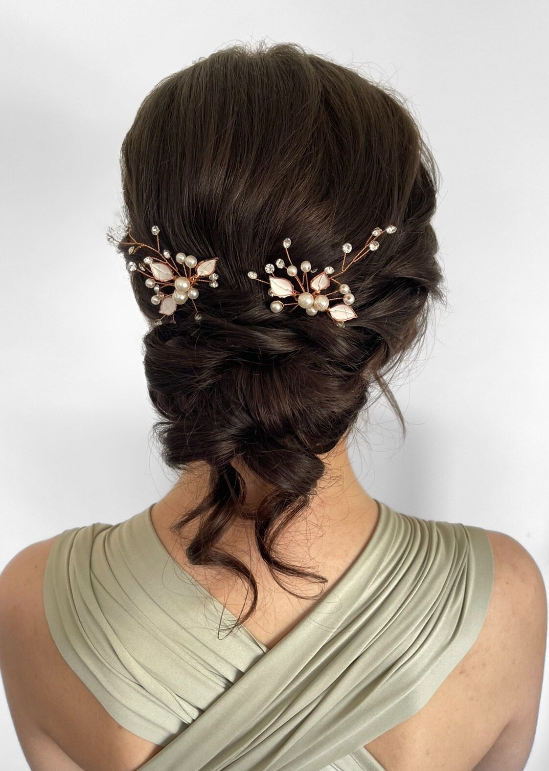 Dark long brunette hair in a loos curled back low bun with soft pieces hanging out detailed with floral accessories