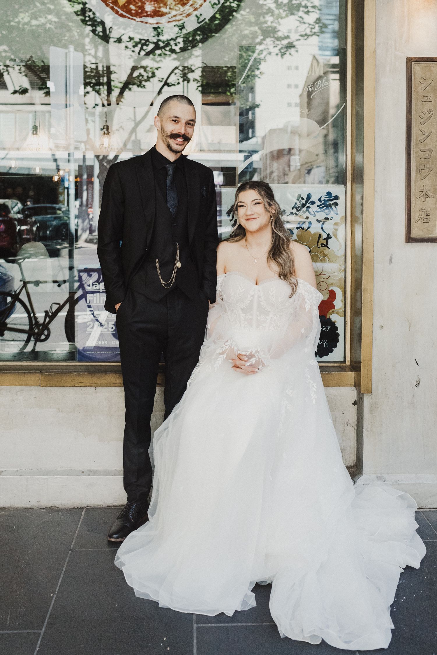 Bride and groom I front of restaurant bride has a soft wave curl half up half down style with slight face framing