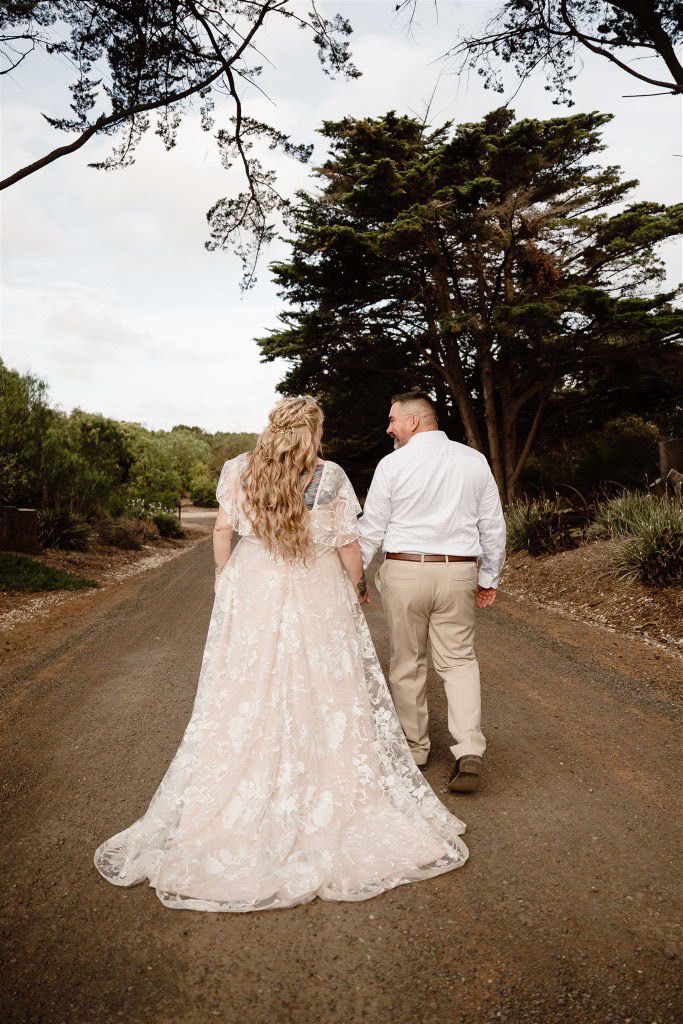 Bride walking along beach path with a super textured tight curl half up half down bridal style pinned back in twists using extensions