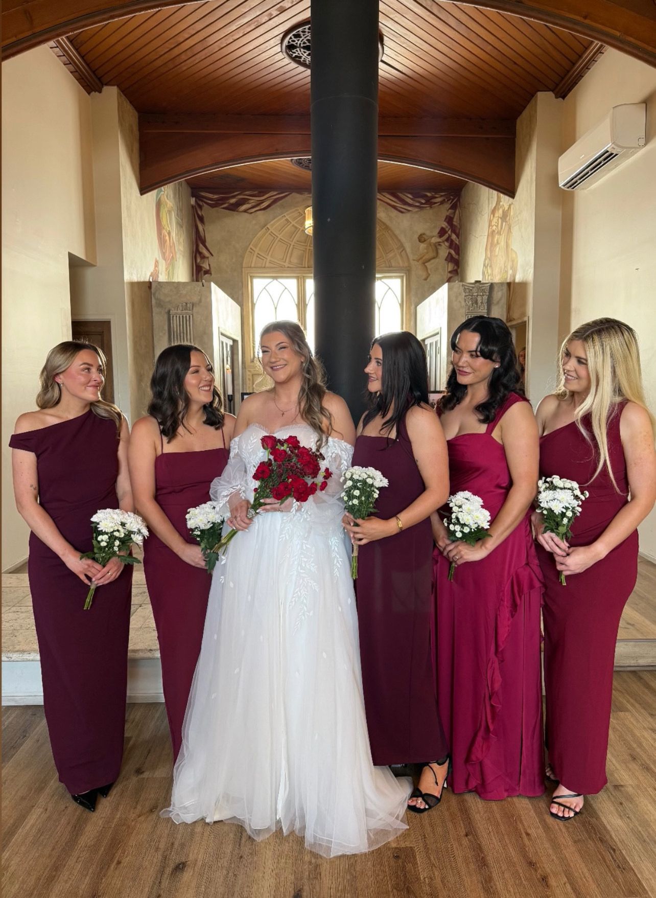 Bridal party in burgundy dresses all with soft flowing waves in their hair and the bride has a boho soft wave half up half down