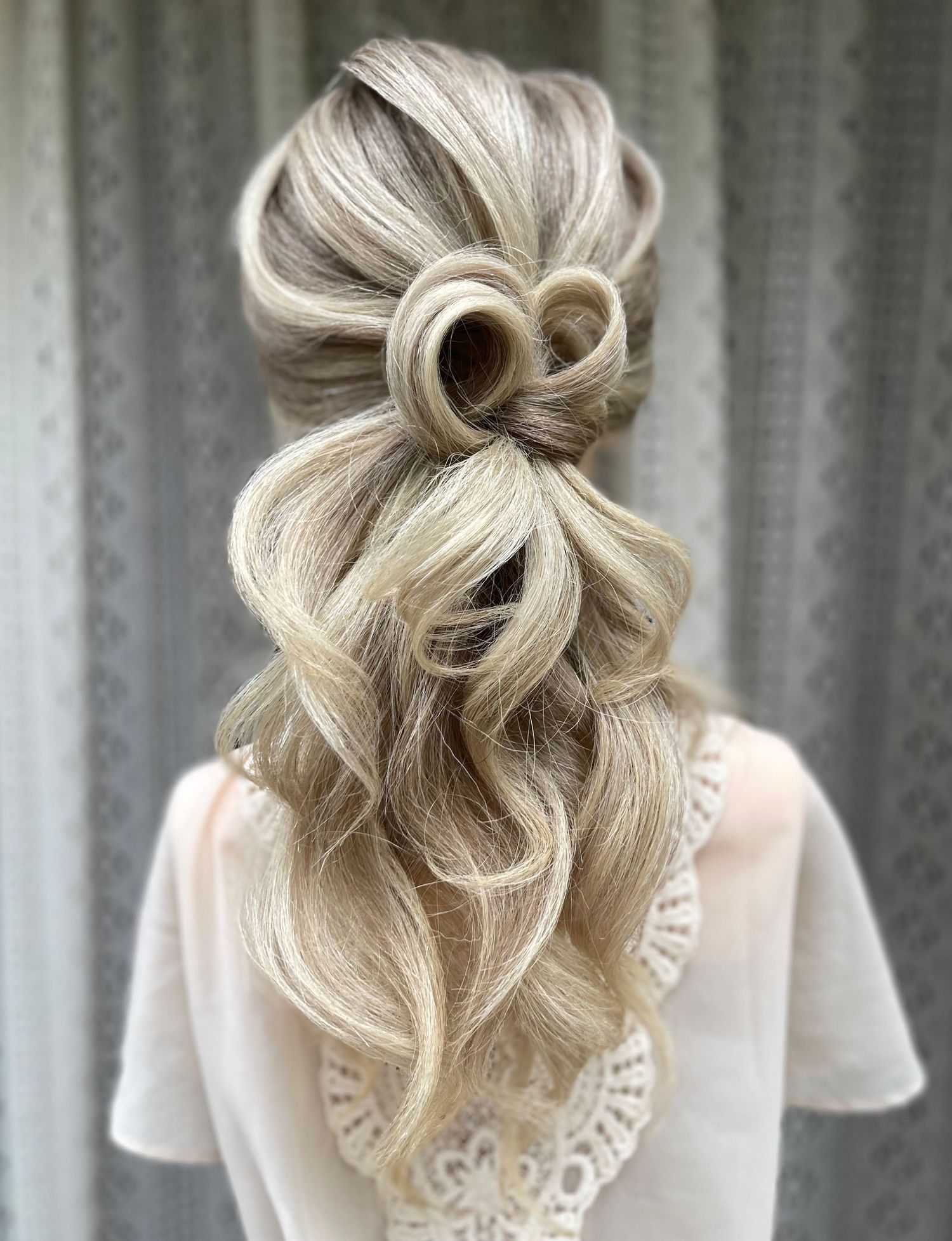 Long blonde hair pulled into a textured pony with two pin curls at the back, with a big volumes curl pony