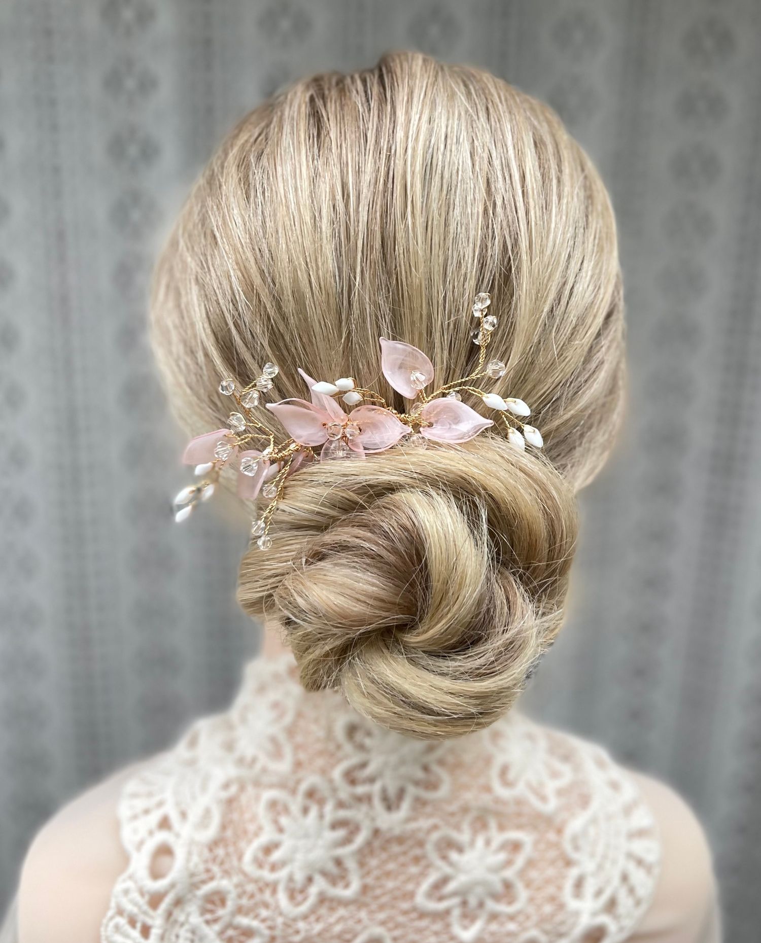 Long blonde hair softly taken back into a twisted low bun detailed with pink floral access