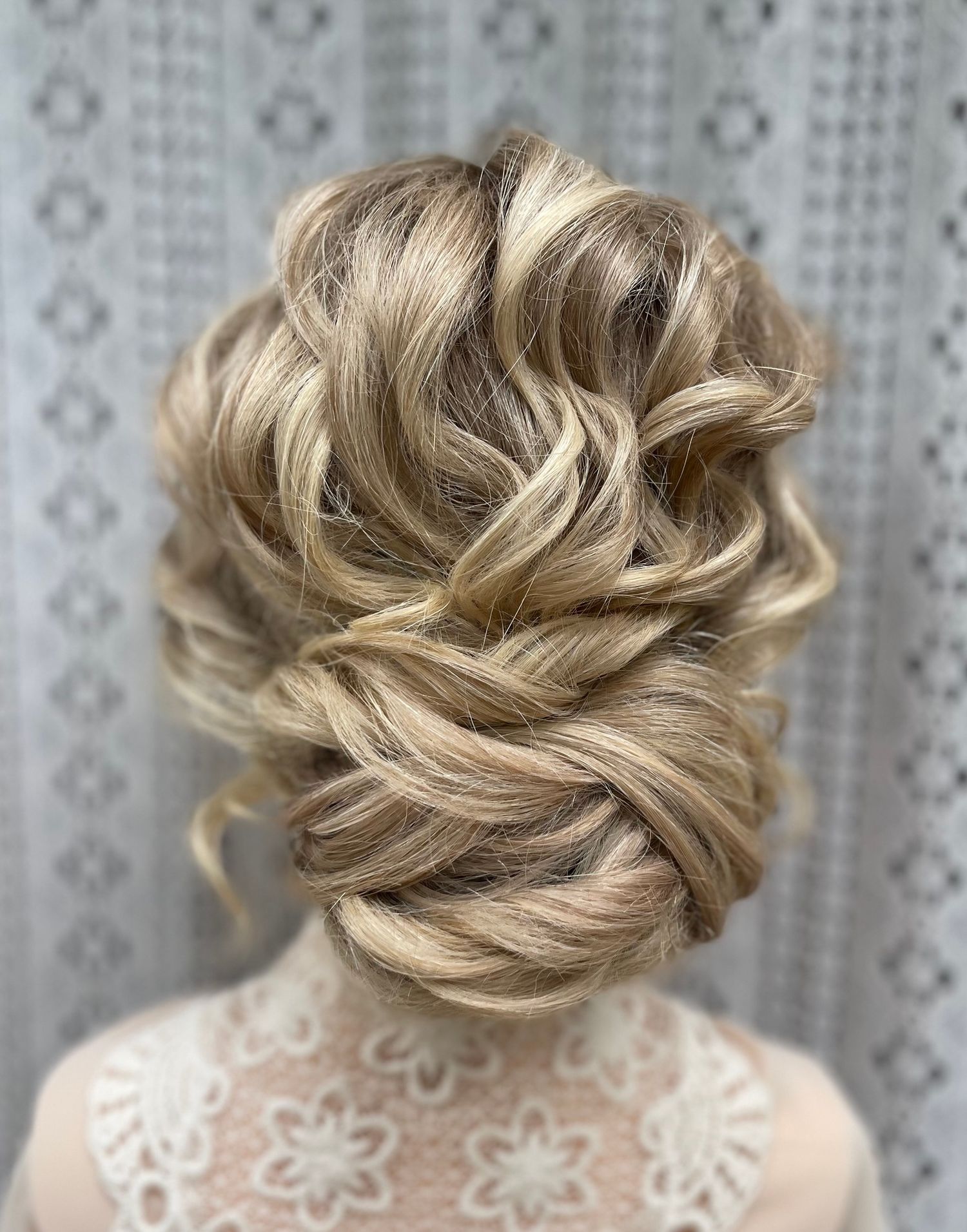 Very textured curly hair in a low twisted bun with curly face framing. Hair is blonde long and thick