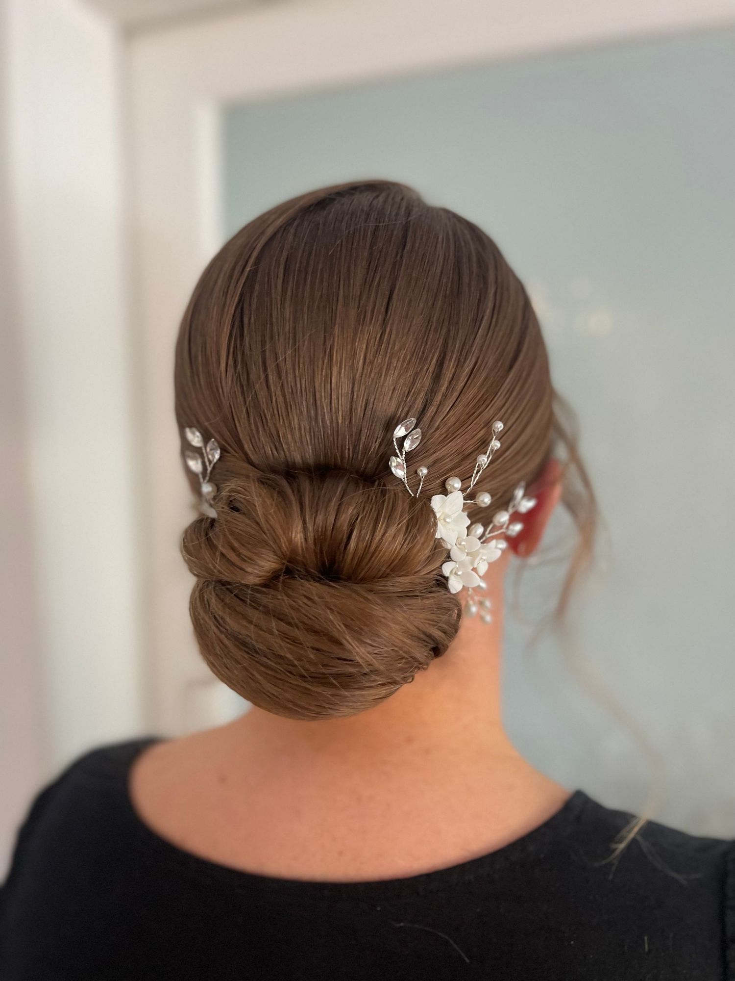 Neat slicked bridal hair style low bun twisted into bun detailed with diamond and floral hair accessories