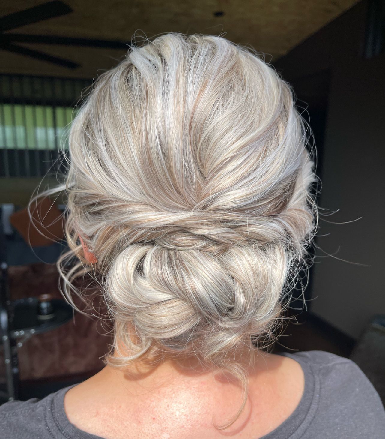 Fine long blonde hair twisted back into a textured low bun with soft face framing for a boho look