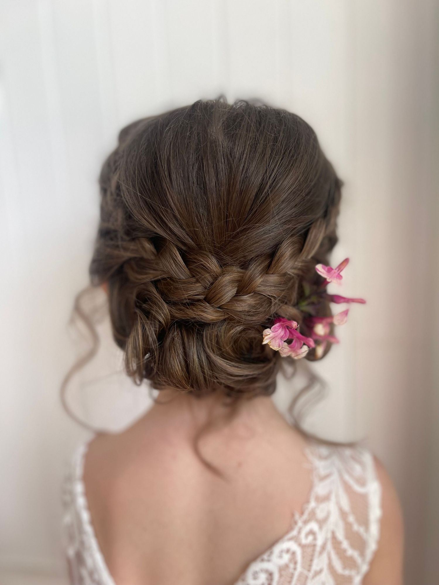 Flower girl hair style in a textured low bun with curled details hanging out styled with fresh flowers