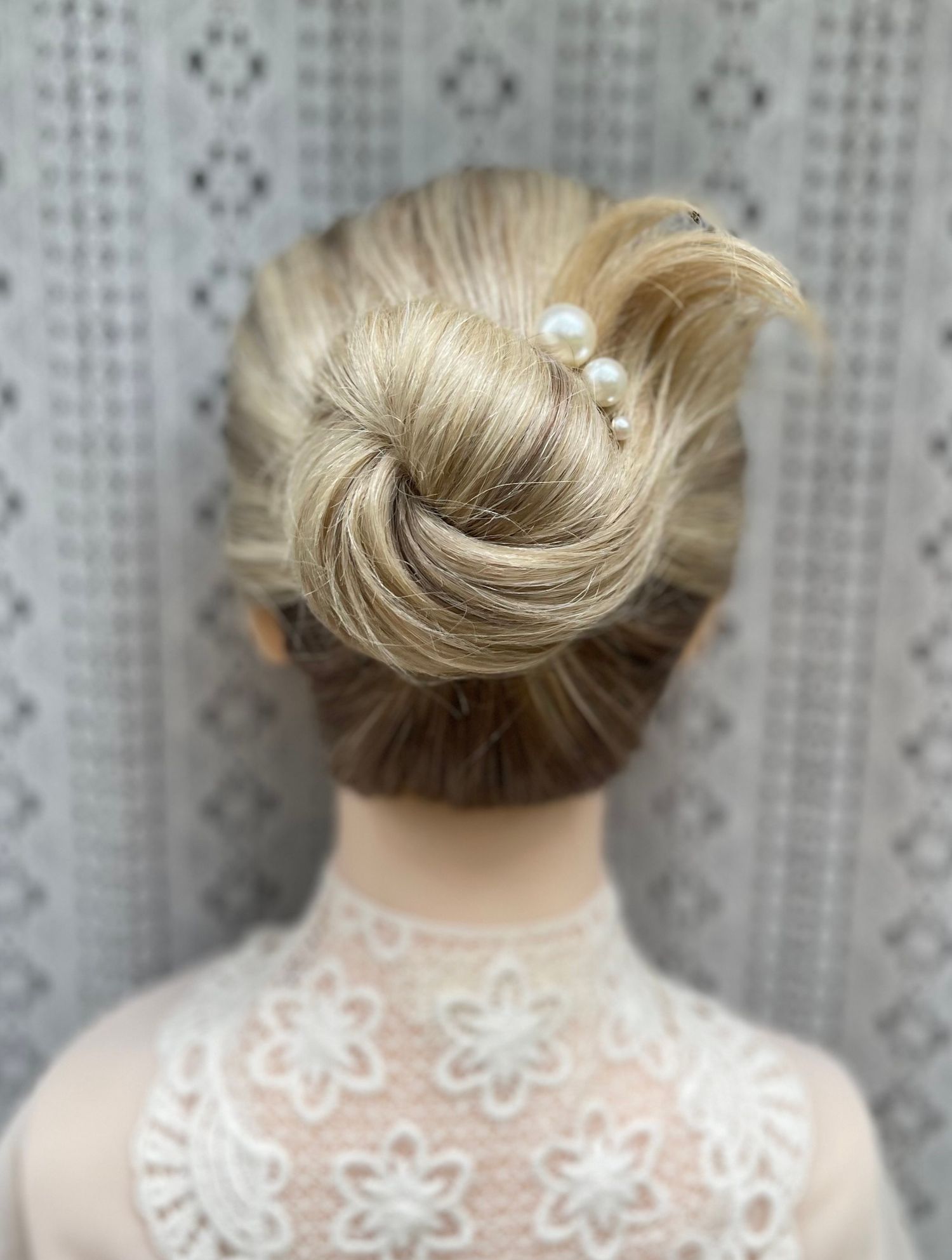 Long thick blonde hair neatly twisted into a high bun with pearl accessories a very neat and elegant bridal look