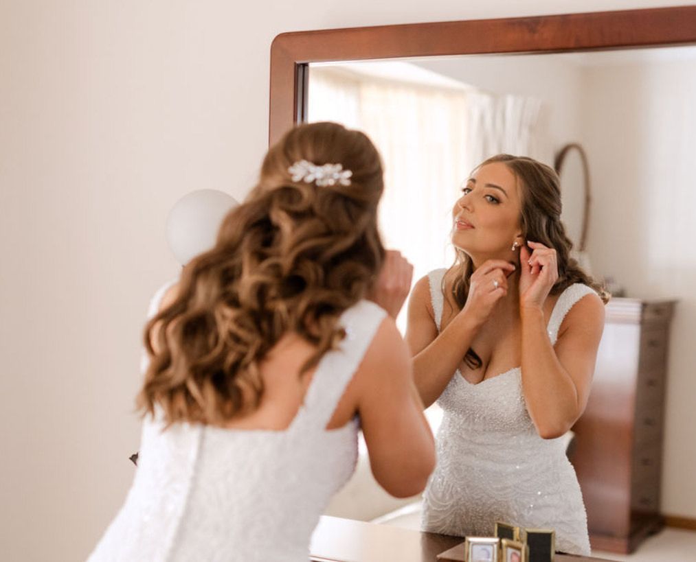 Bride looking into mirror adjusting earrings with long thick brunette hair in a high shine Hollywood wave and a vintage diamond hair clip