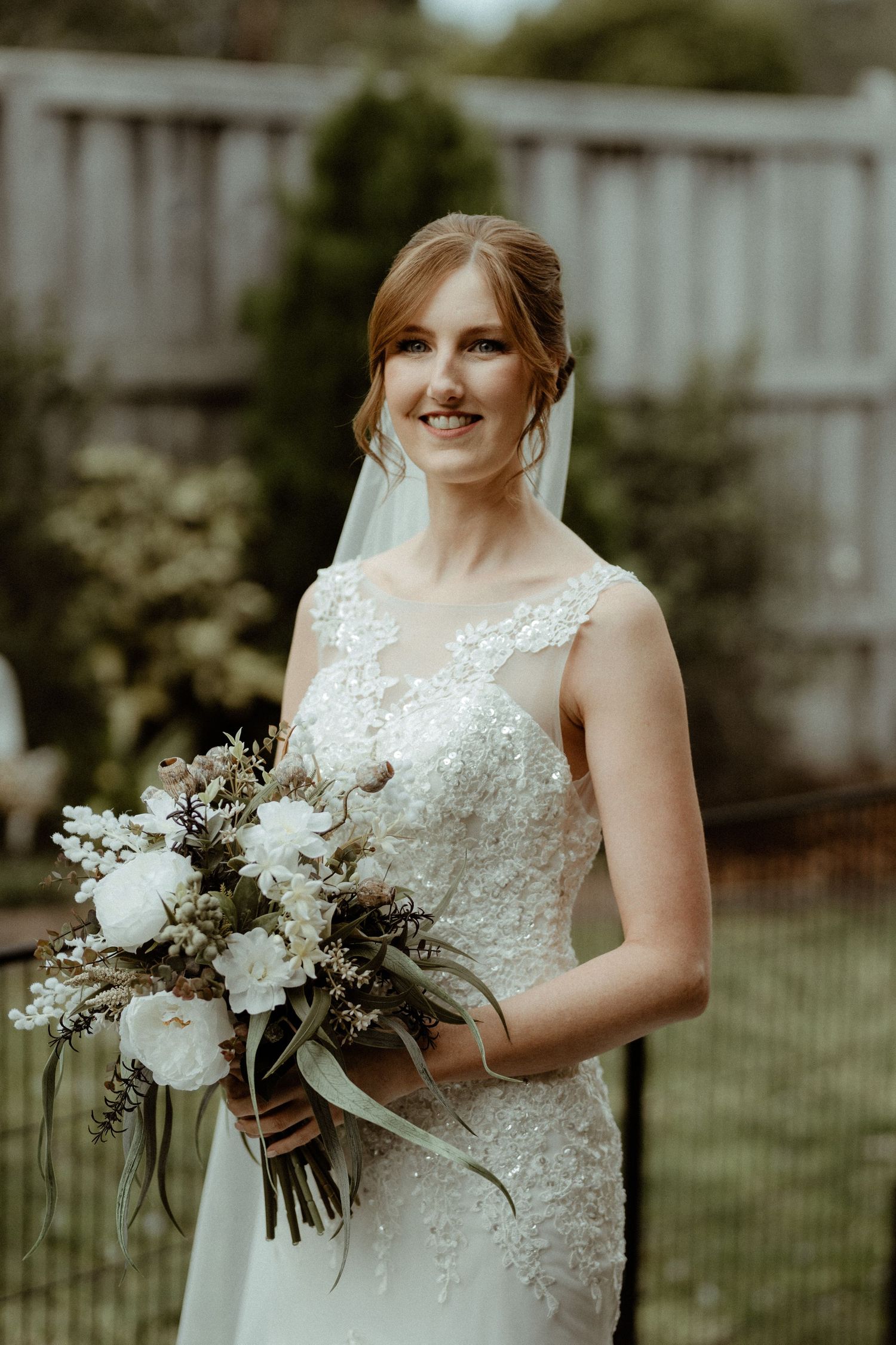 Red hair bride with long thick hair in neat low bun with soft face framing wearing a veil in a garden setting
