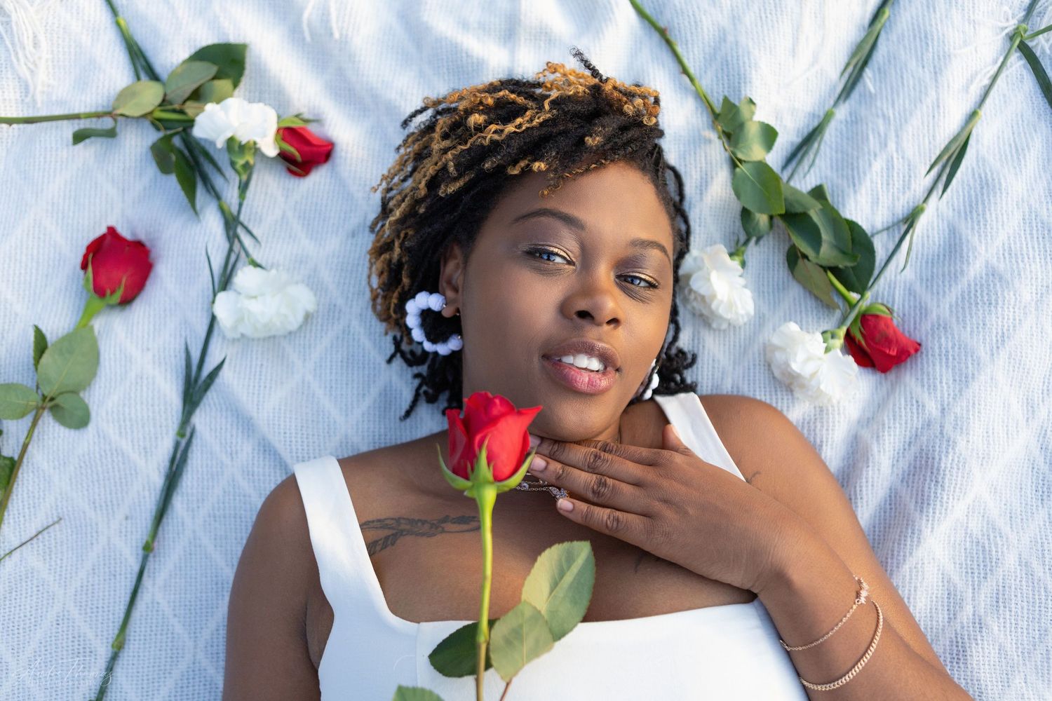 vibrant day of model laying in on a white blanket surounded by roses.