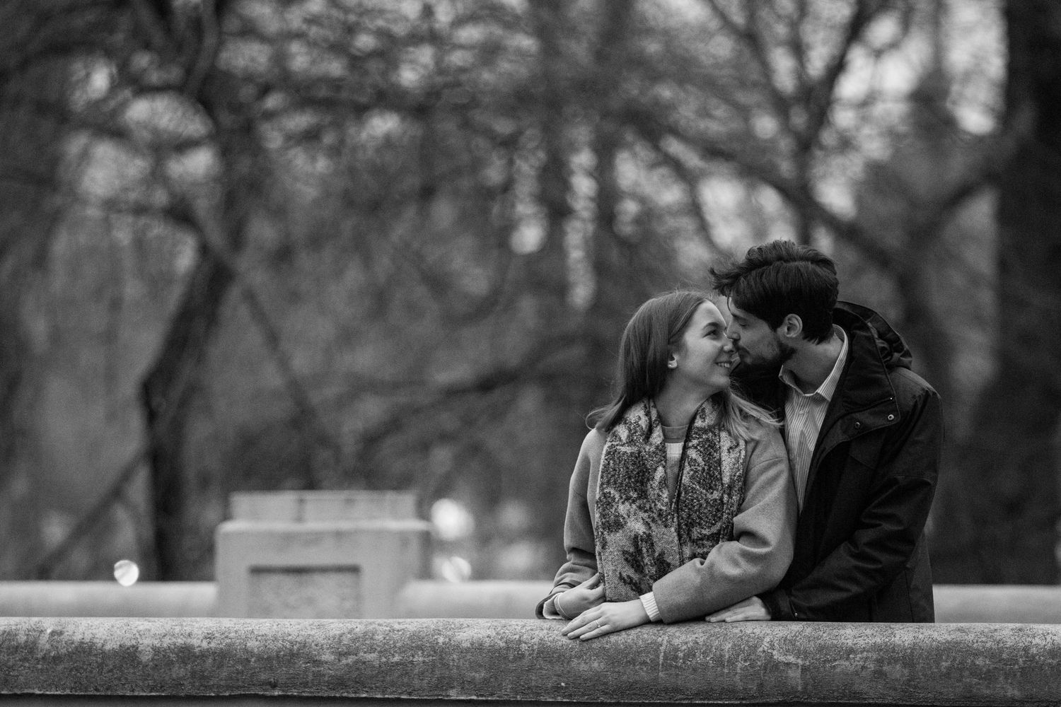 Black and white photo of a couple lying together on a stone wall in a park.