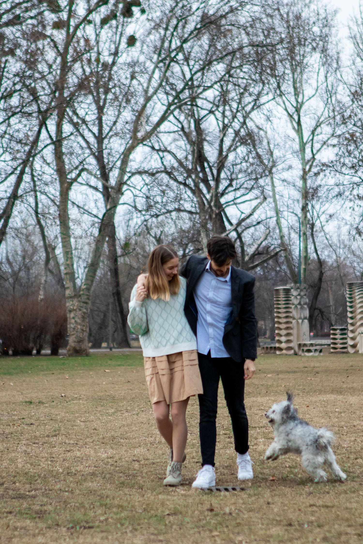 A couple poses with their fluffy white dog in a park setting.