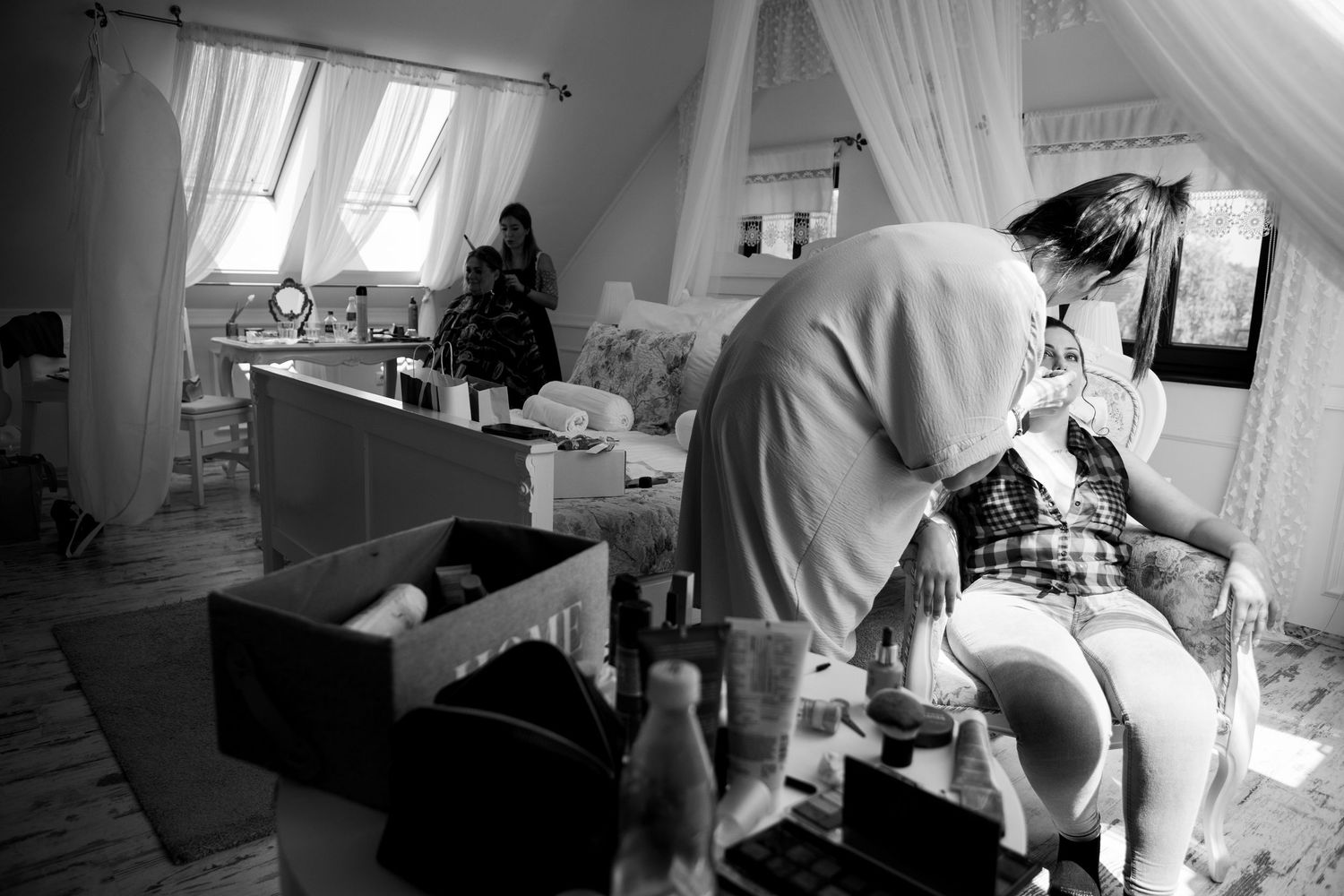Black and white photo of wedding preparation in a sunlit room with flowing curtains.