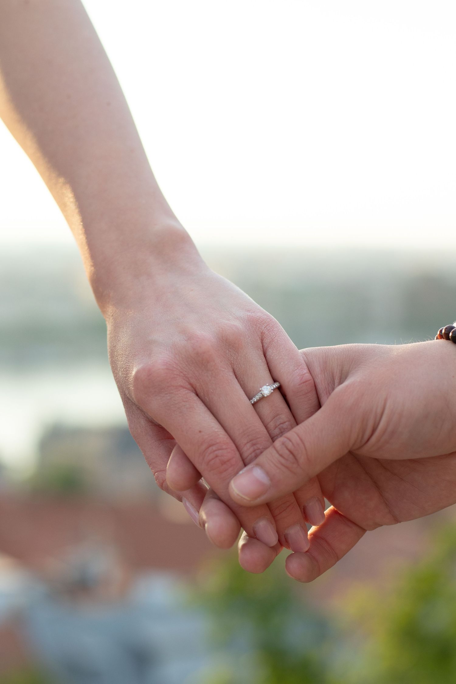 Close-up shots of hands with engagement rings intertwined against a blurred outdoor background.