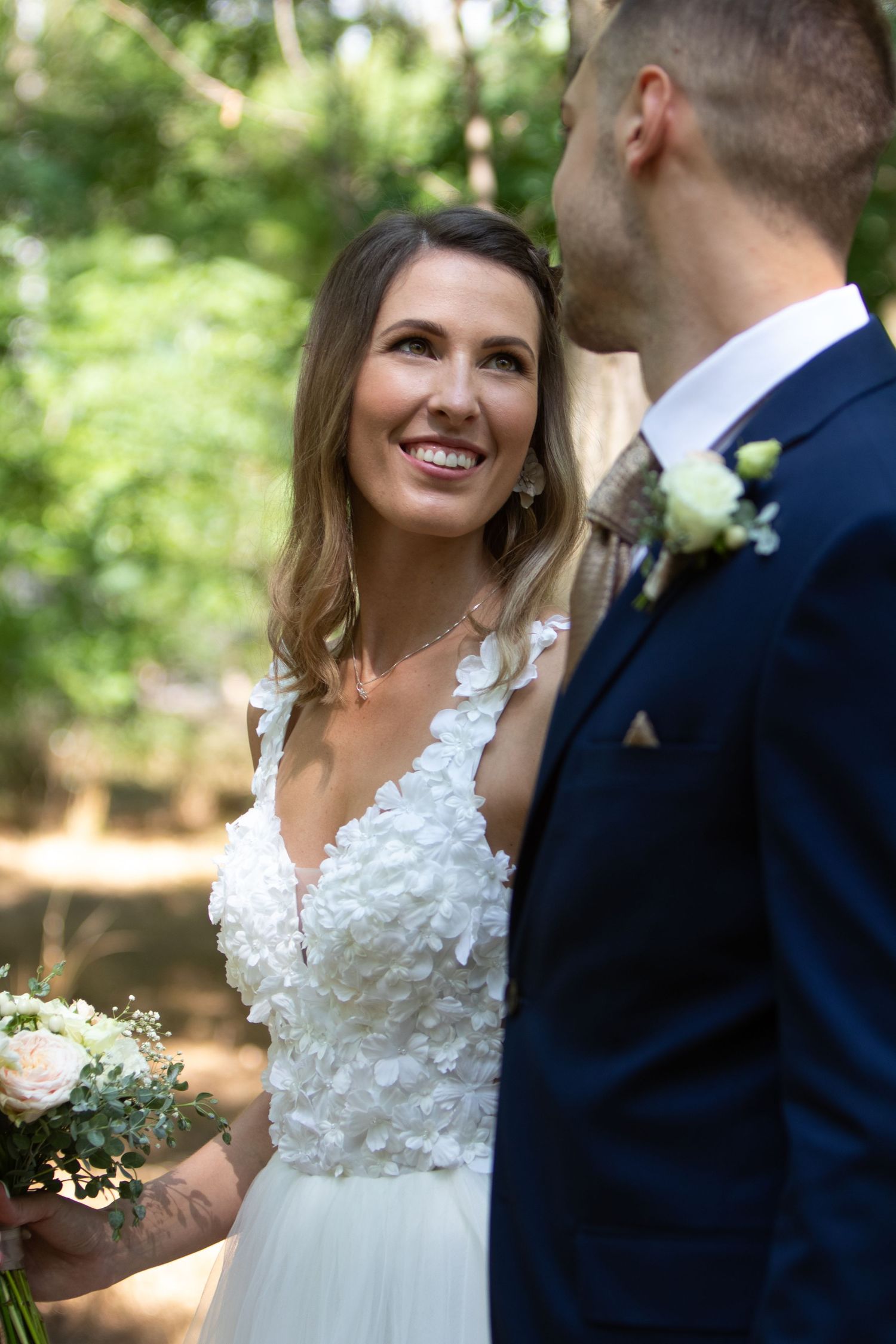 Outdoor wedding scene with couple in formal attire among green foliage.