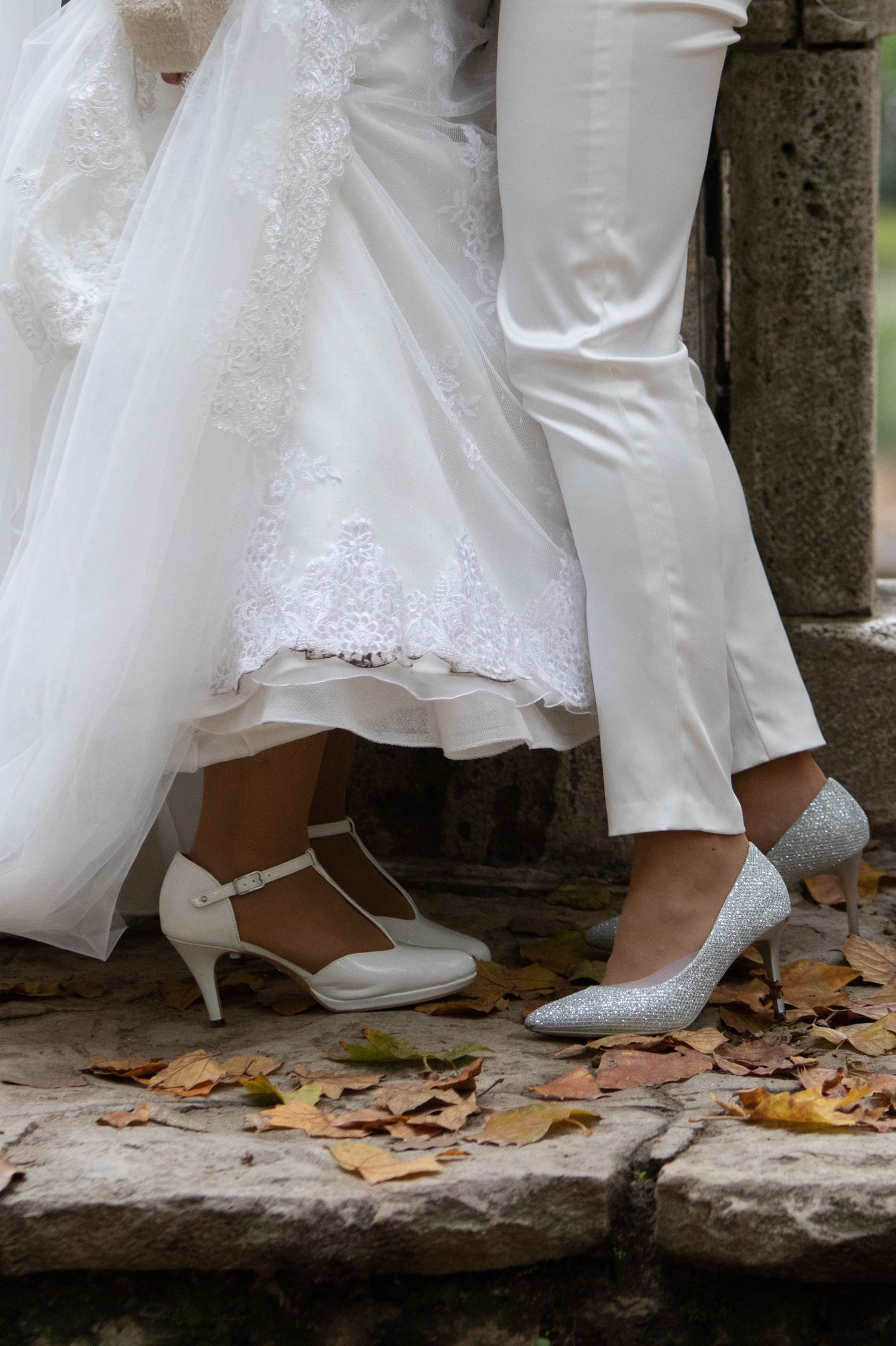 Detail shot of white wedding dress and shoes on stone steps with autumn leaves.