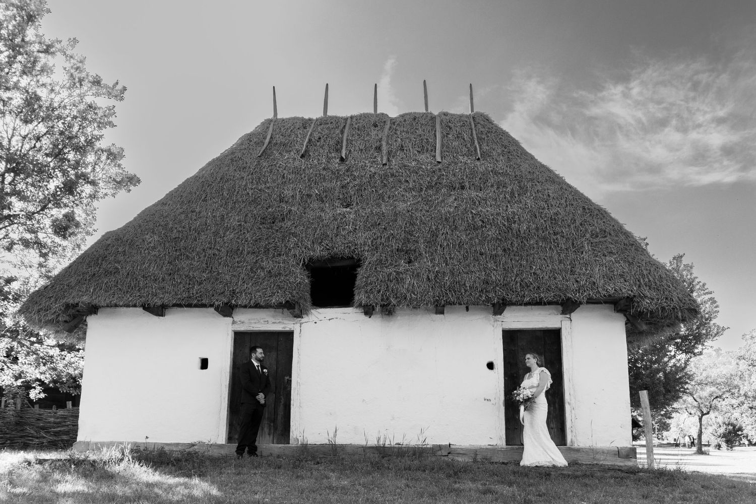 Black and white photo of traditional thatched roof cottage with wedding couple in doorways.
