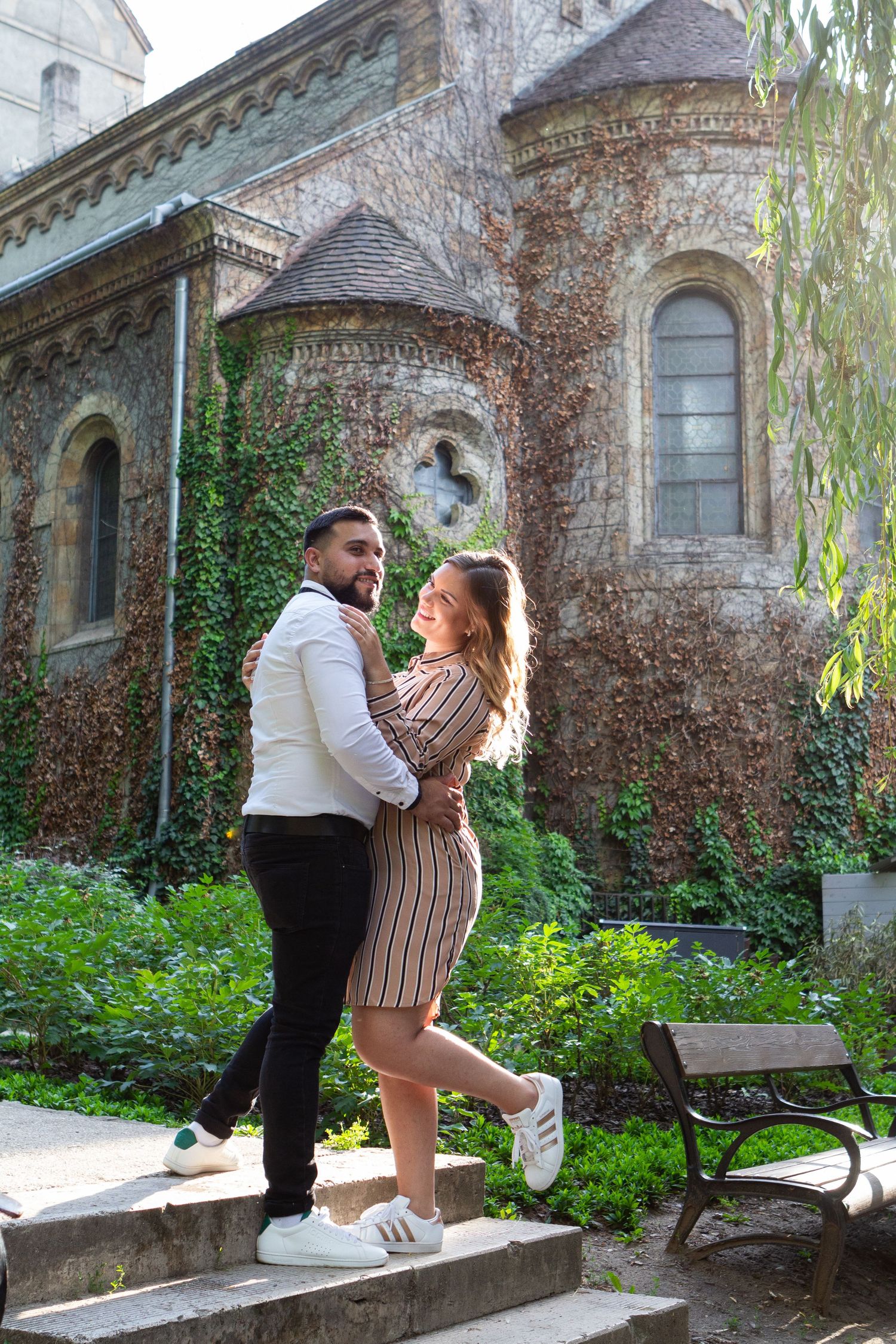 Couple sharing playful moments outside a historic stone building with ivy and gothic architecture.