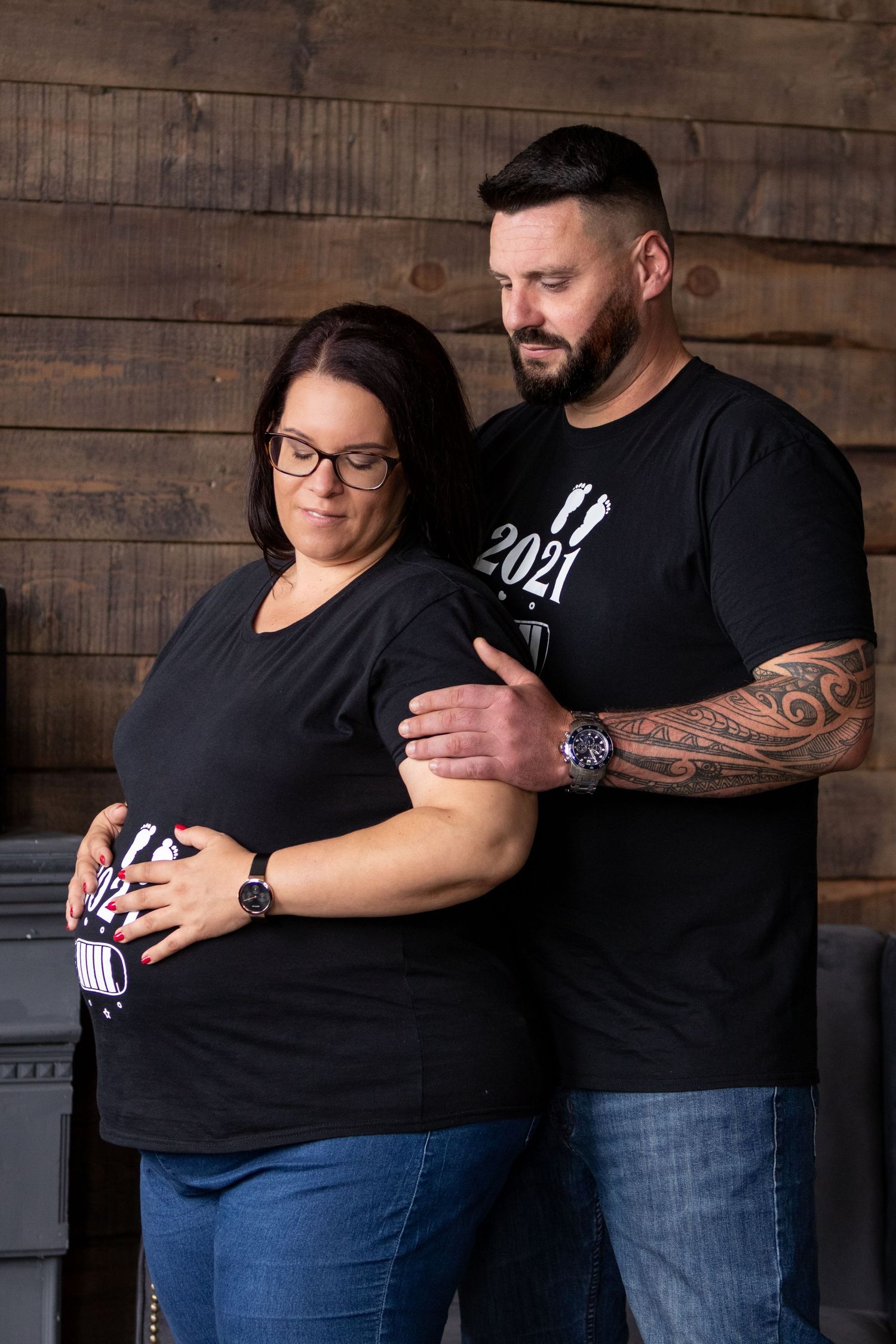 Couple in matching black outfits share intimate moment during indoor maternity photoshoot.