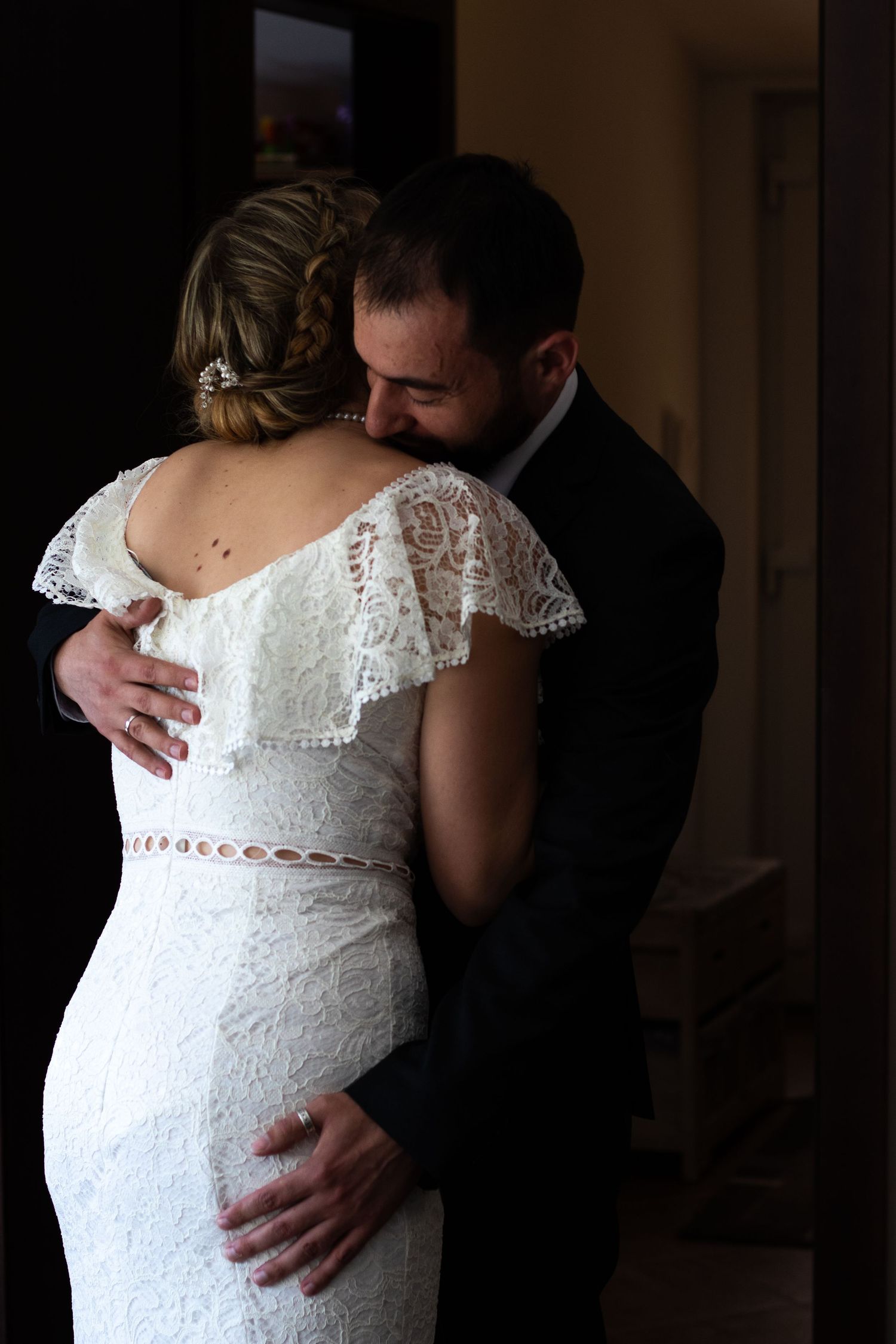 An intimate embrace captured in dramatic lighting showing lace wedding dress details.