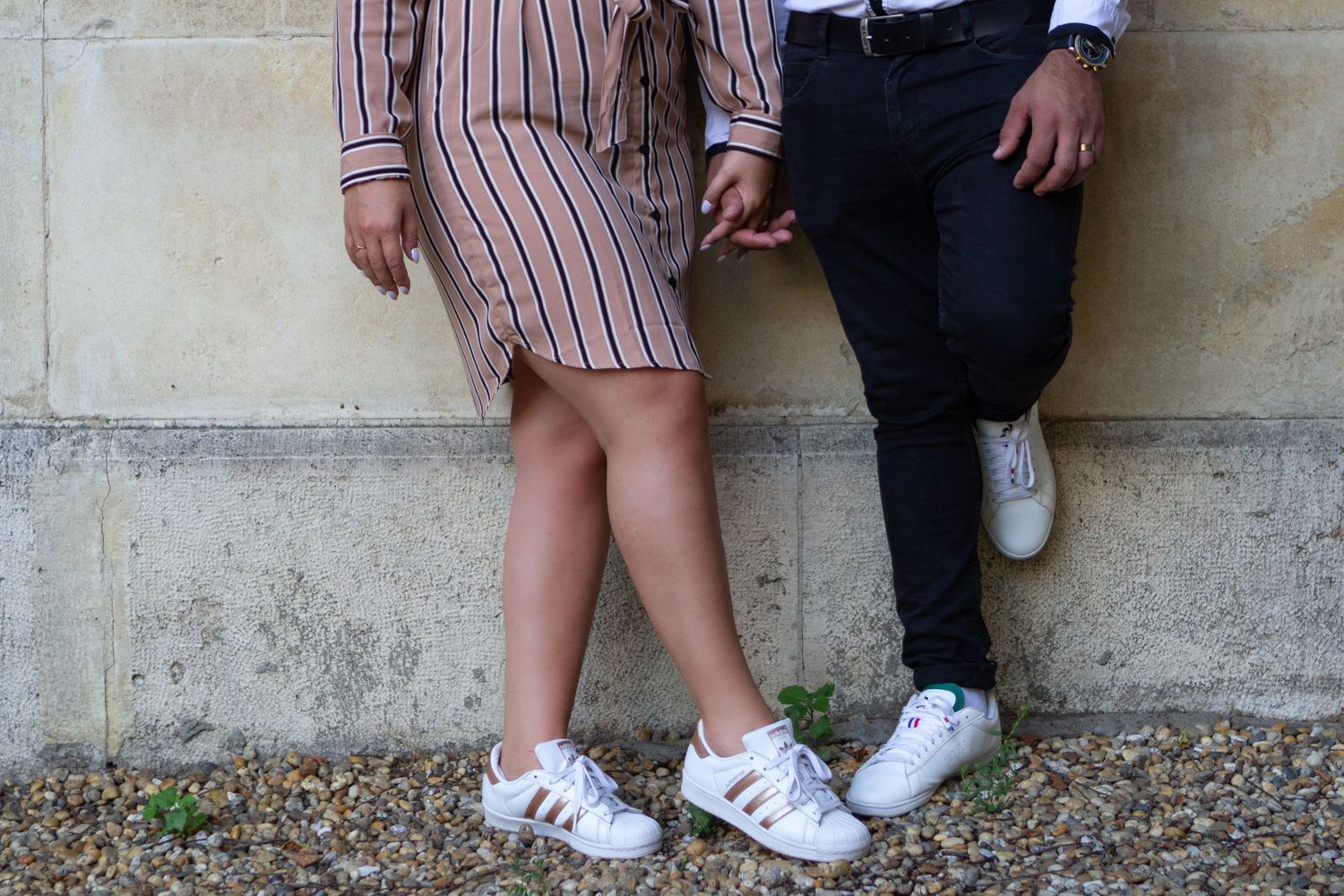 A couple poses playfully against a stone wall in coordinated outfits.