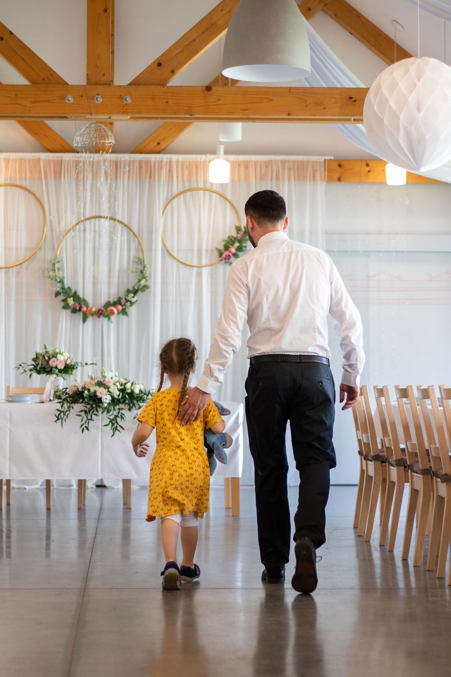 Wedding venue interior with wooden beams and floral hoops decorating a white backdrop.