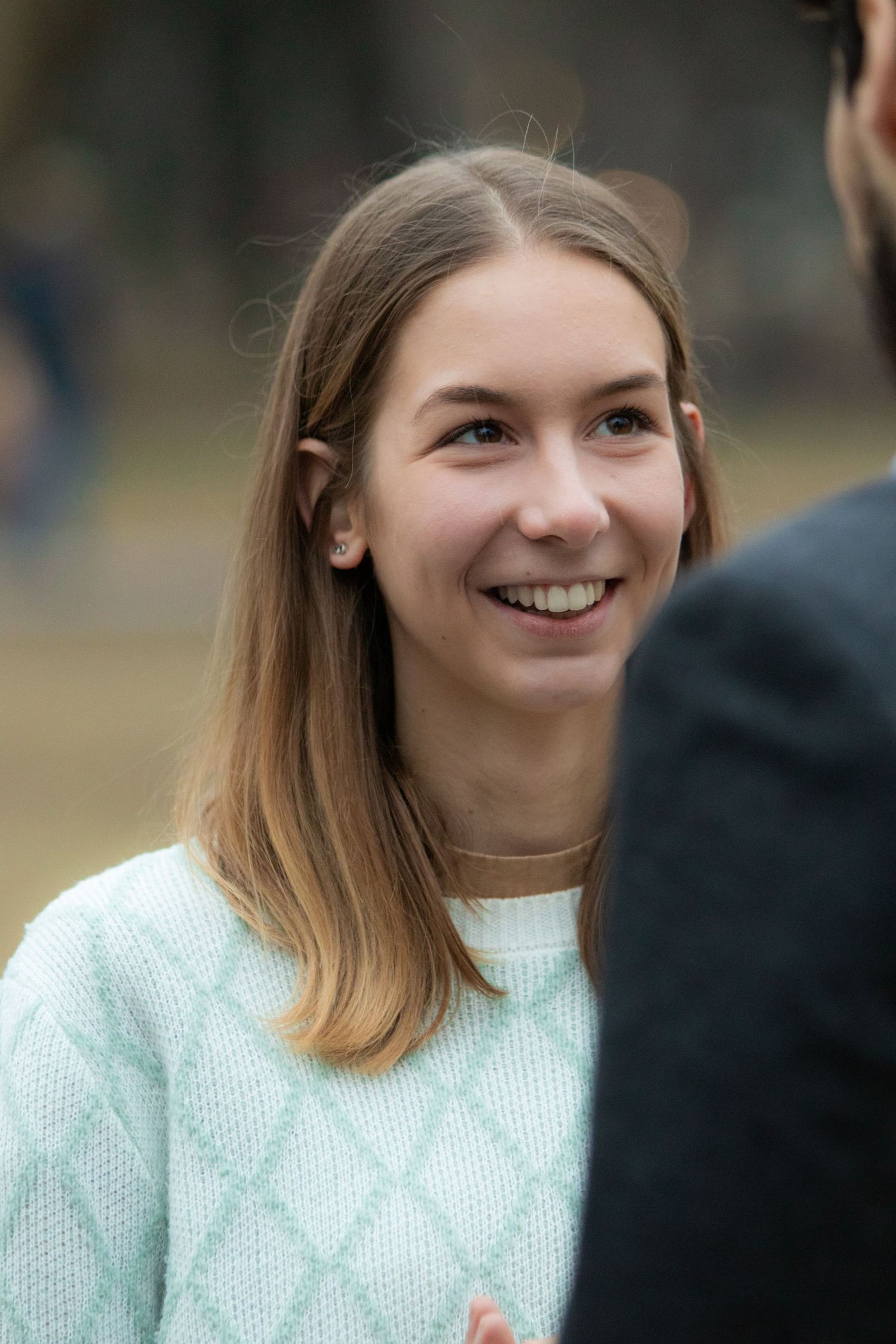Person in white knit sweater smiling warmly during an outdoor photoshoot.