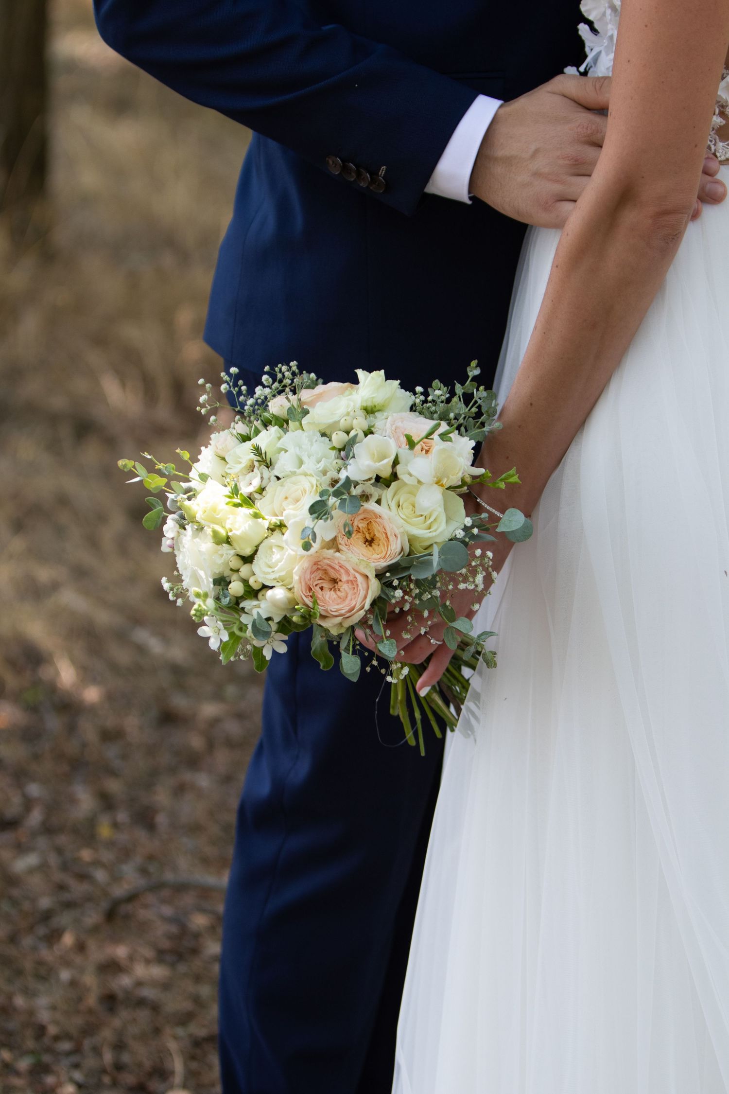 Elegant wedding bouquet with white roses and greenery against formal attire.