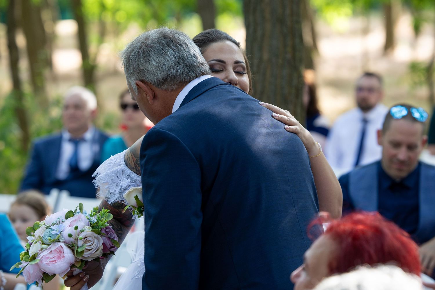 Wedding guests gathering outdoors for photos under tree cover.