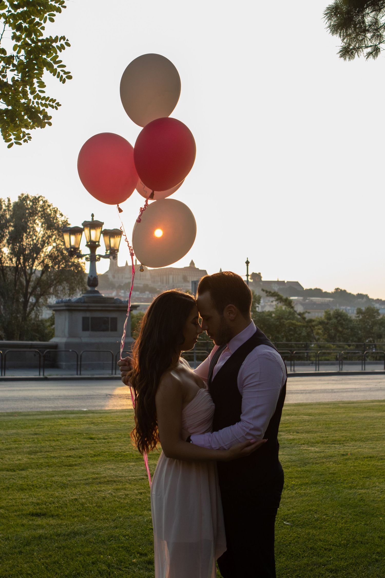 Romantic couple with large balloons embracing in a park during sunset.