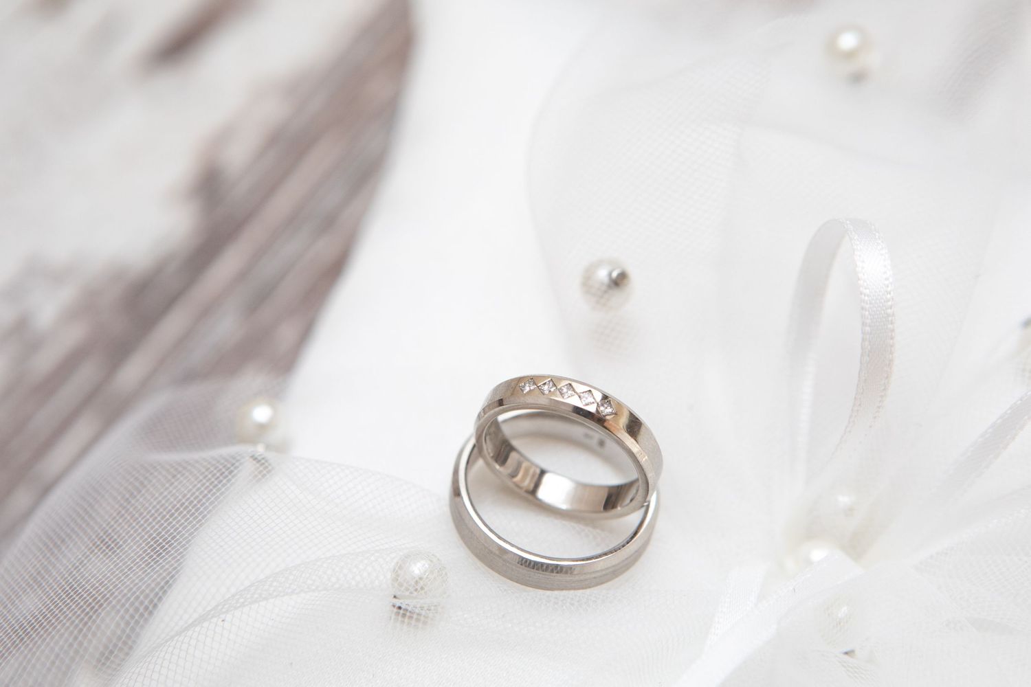 Wedding rings displayed on white tulle fabric with delicate pearl decorations.