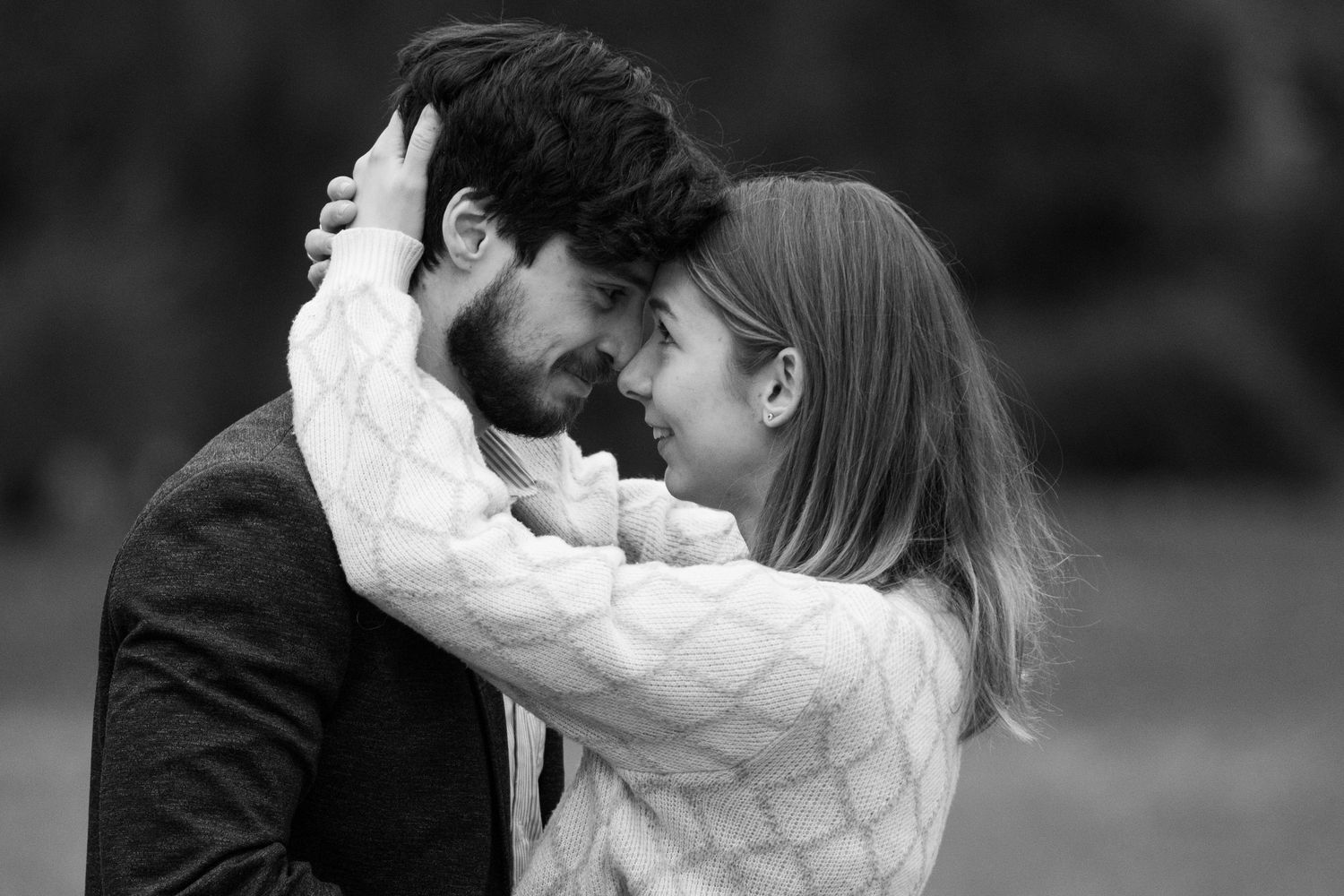 A tender black and white photo of a couple sharing an affectionate moment outdoors.