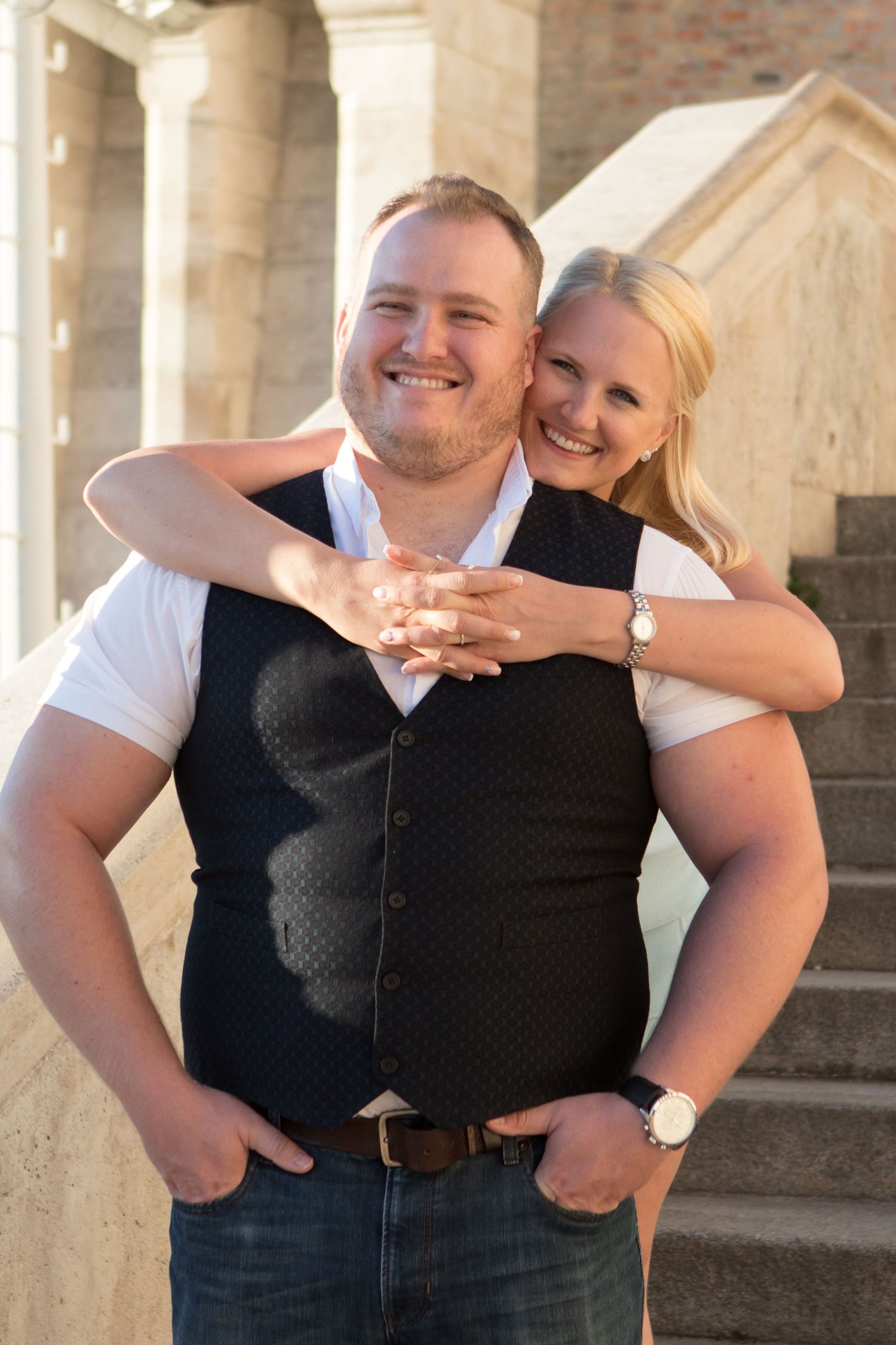Happy couple sharing joyful moments in casual attire against stone architecture.