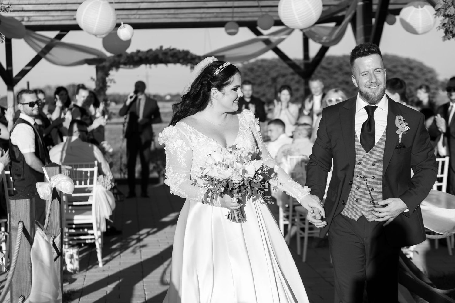 A wedding ceremony takes place under a decorated pavilion with white balloons and gathered guests.