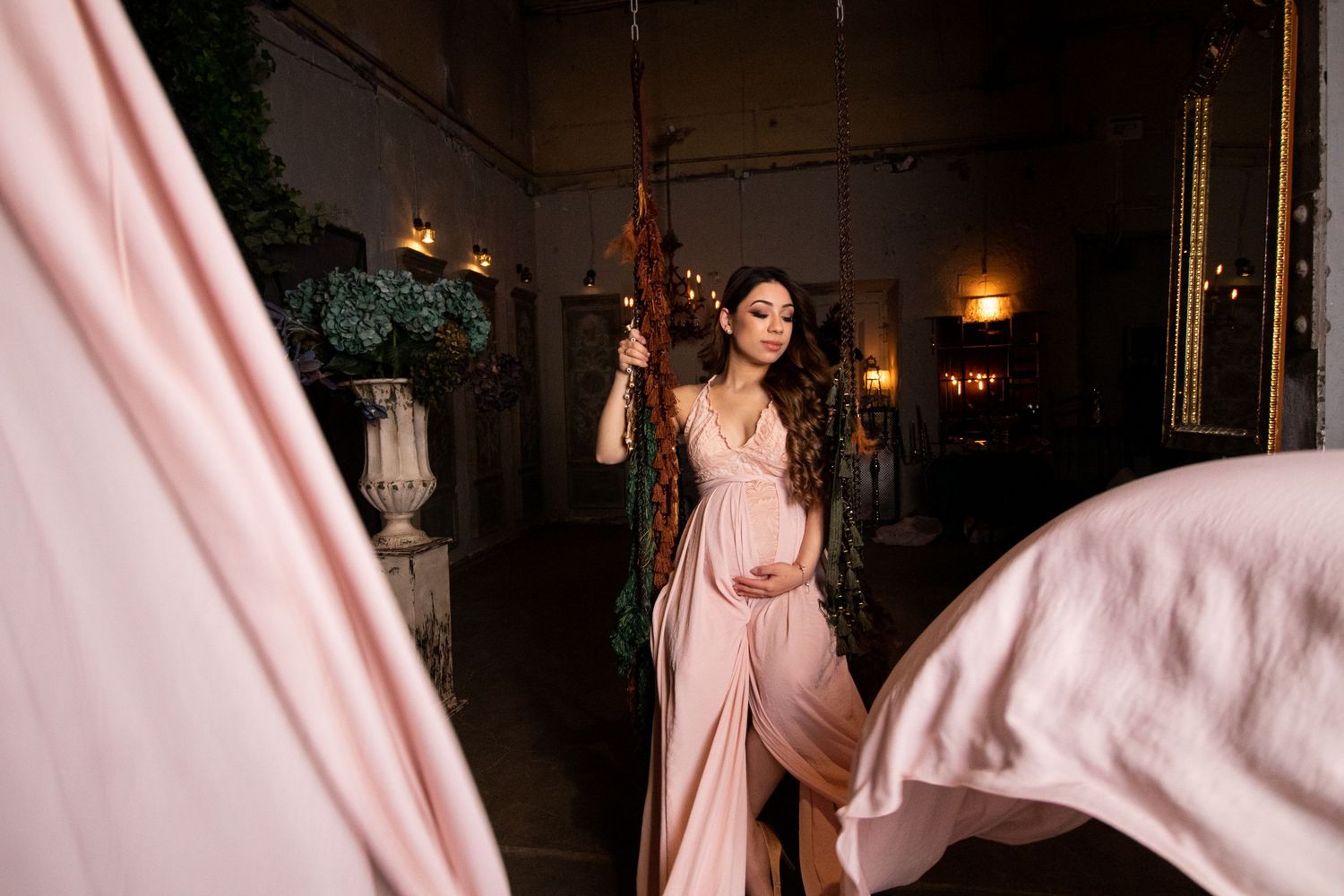 Artistic maternity portraits with flowing pink fabric in elegant indoor setting.